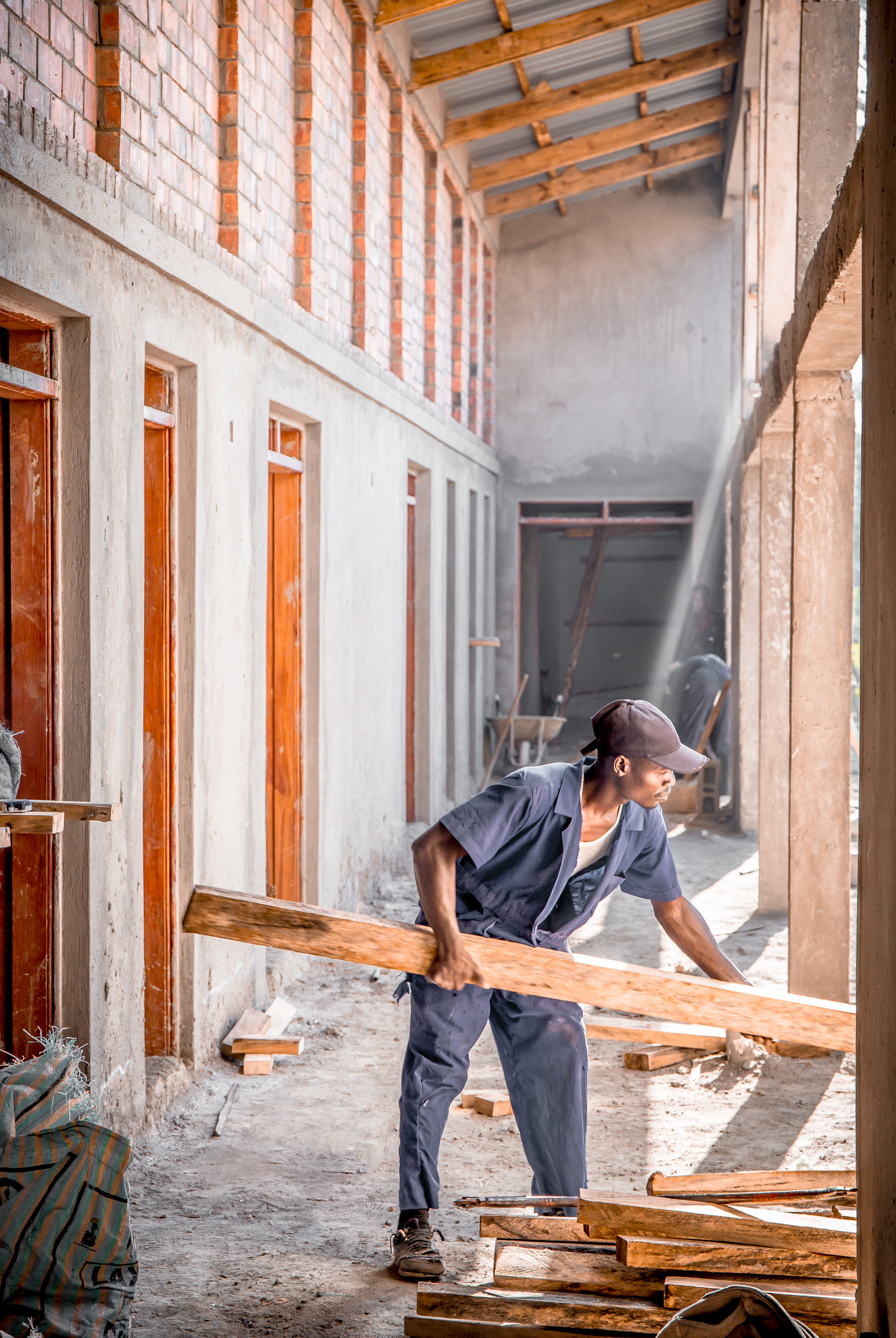 Worker carrying timber planks through a double-height courtyard with exposed concrete walls and wooden window frames