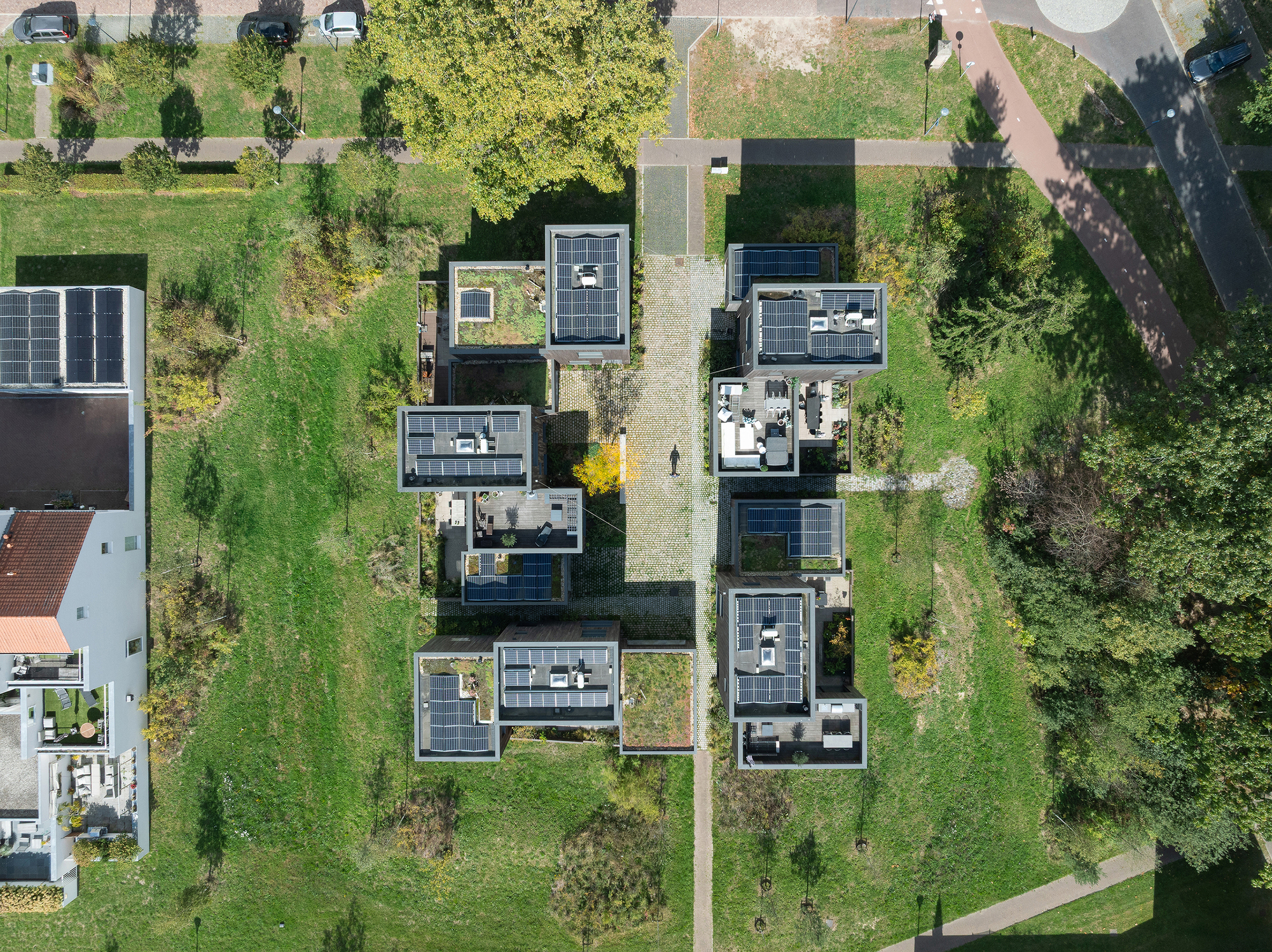 Aerial view of timber houses with photovoltaic panels arranged along a central pathway through green lots
