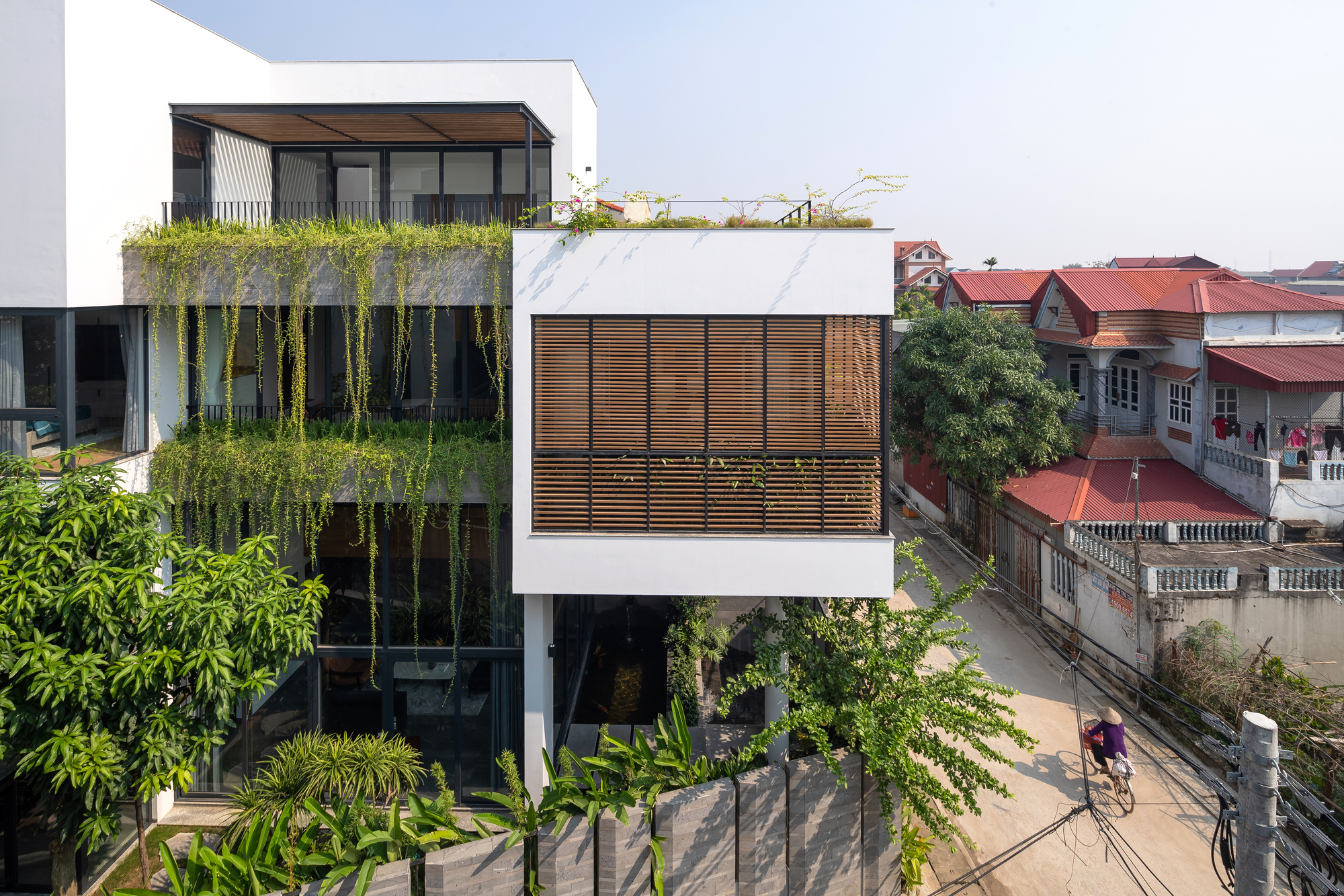Street elevation showing stacked volumes with timber screens, cascading planters, and cyclists passing below