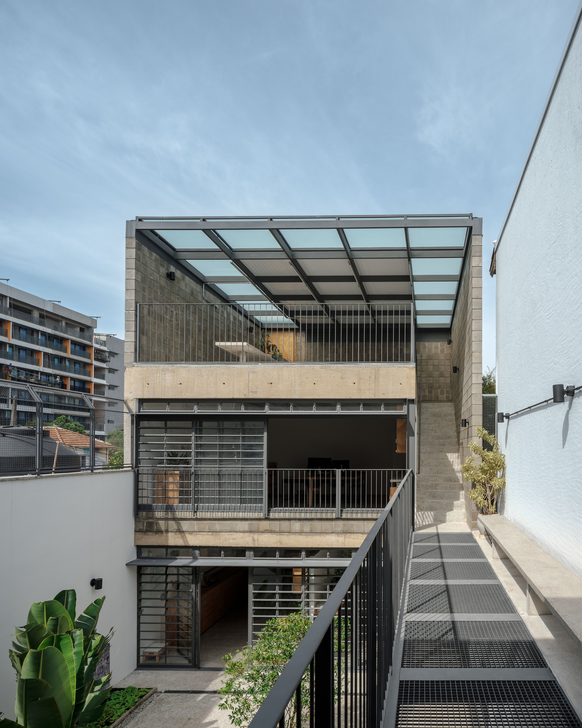 Courtyard view showing stacked terraces with glass canopy, perforated metal balustrades, and metal mesh walkway