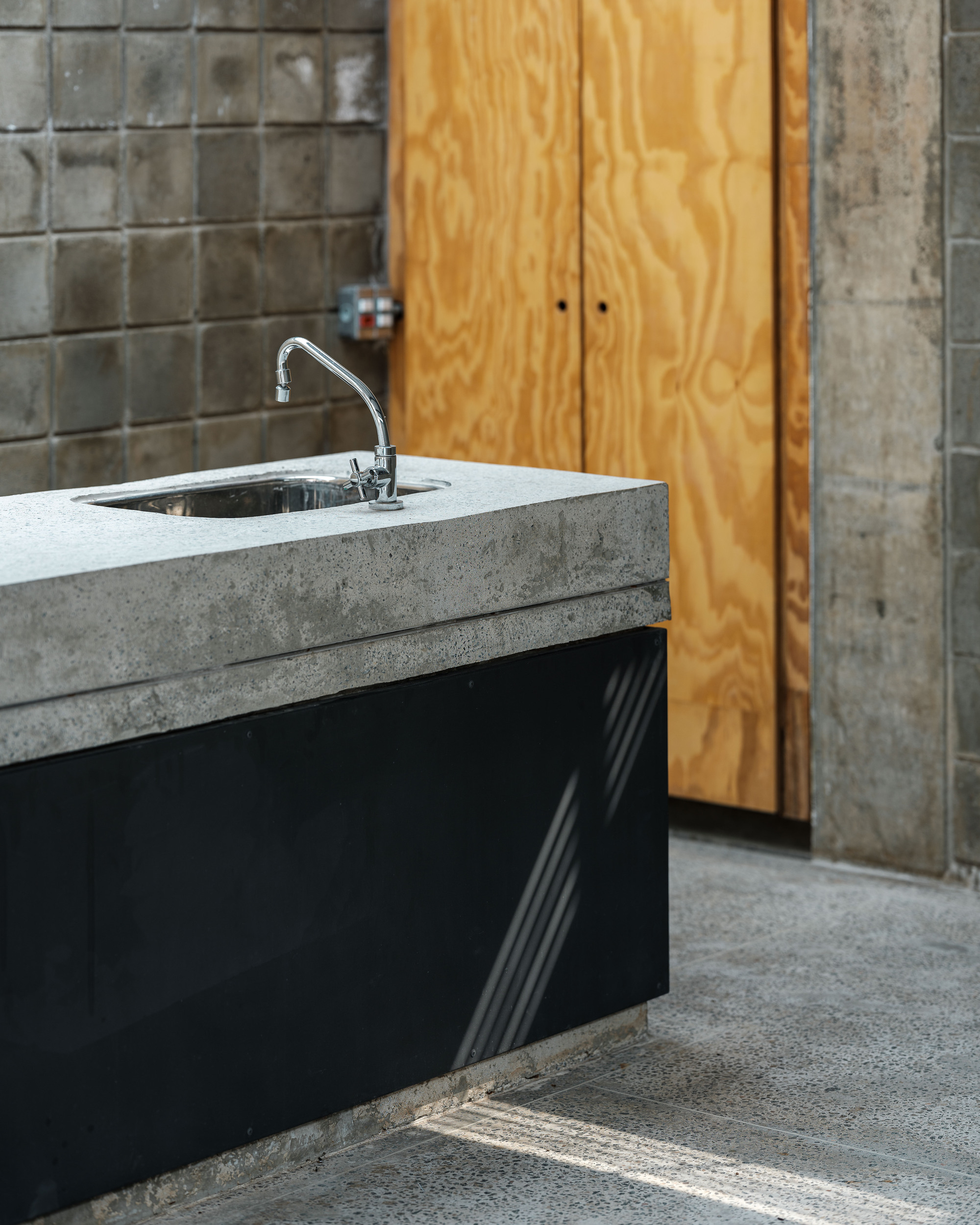 Concrete countertop with stainless steel sink against glazed tile wall and plywood cabinet doors