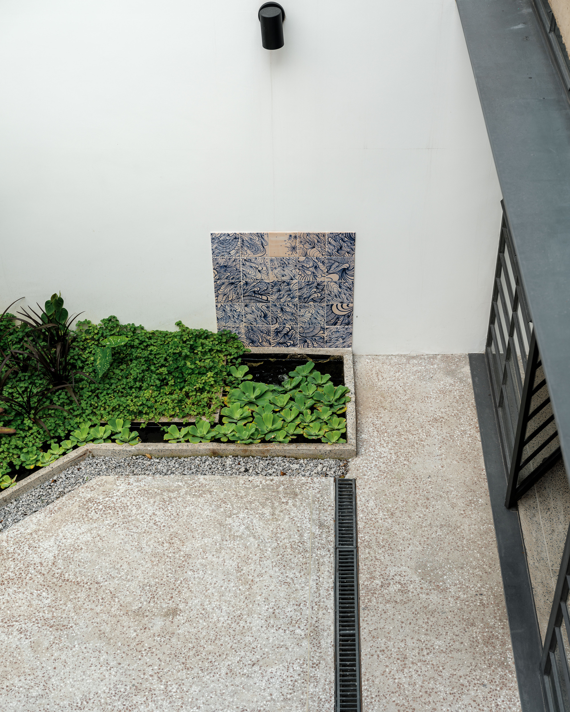 Top-down view of courtyard with planted bed, exposed aggregate paving, and patterned tile wall panel