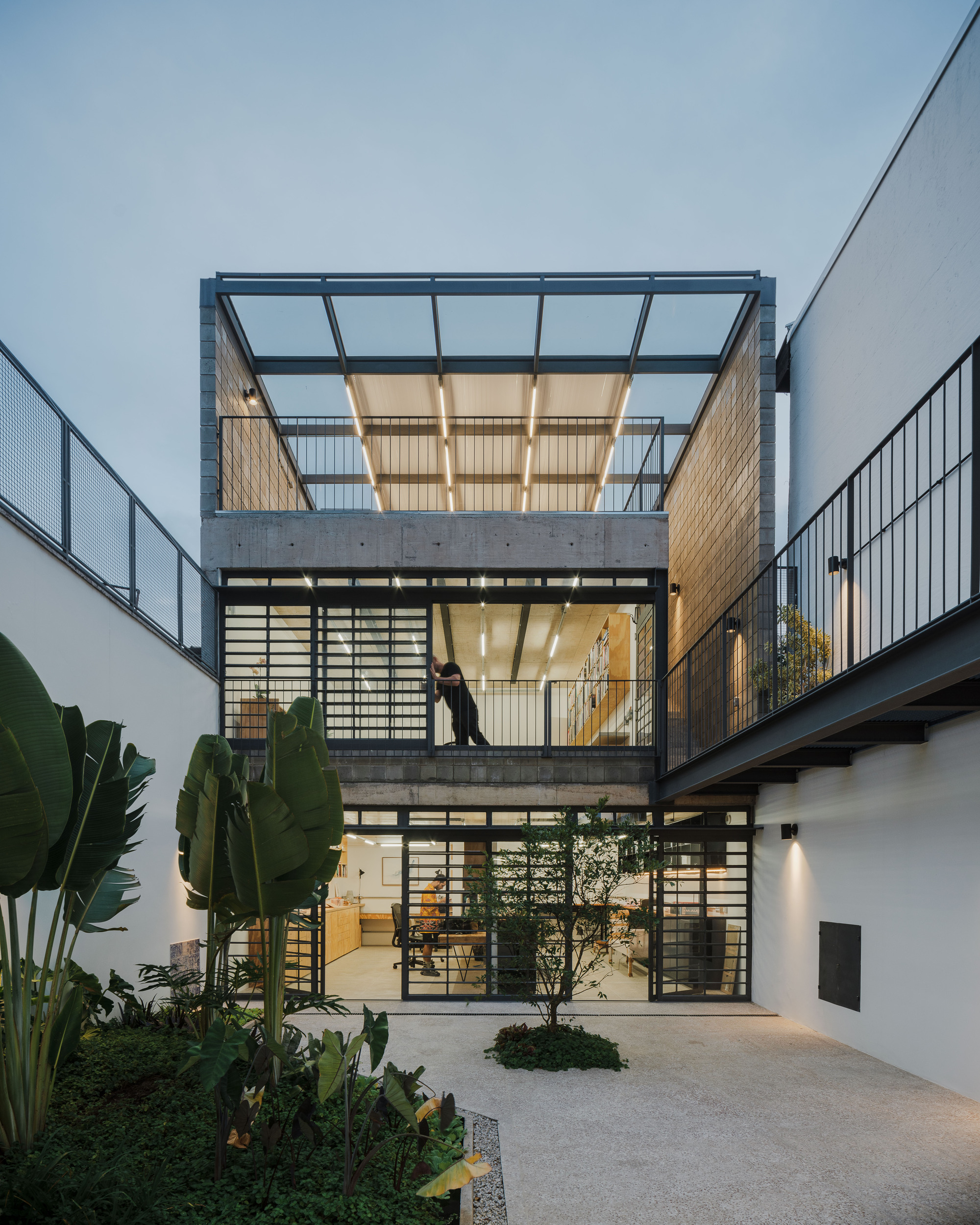 Three-story courtyard elevation at dusk with person visible on middle level and banana palms in foreground