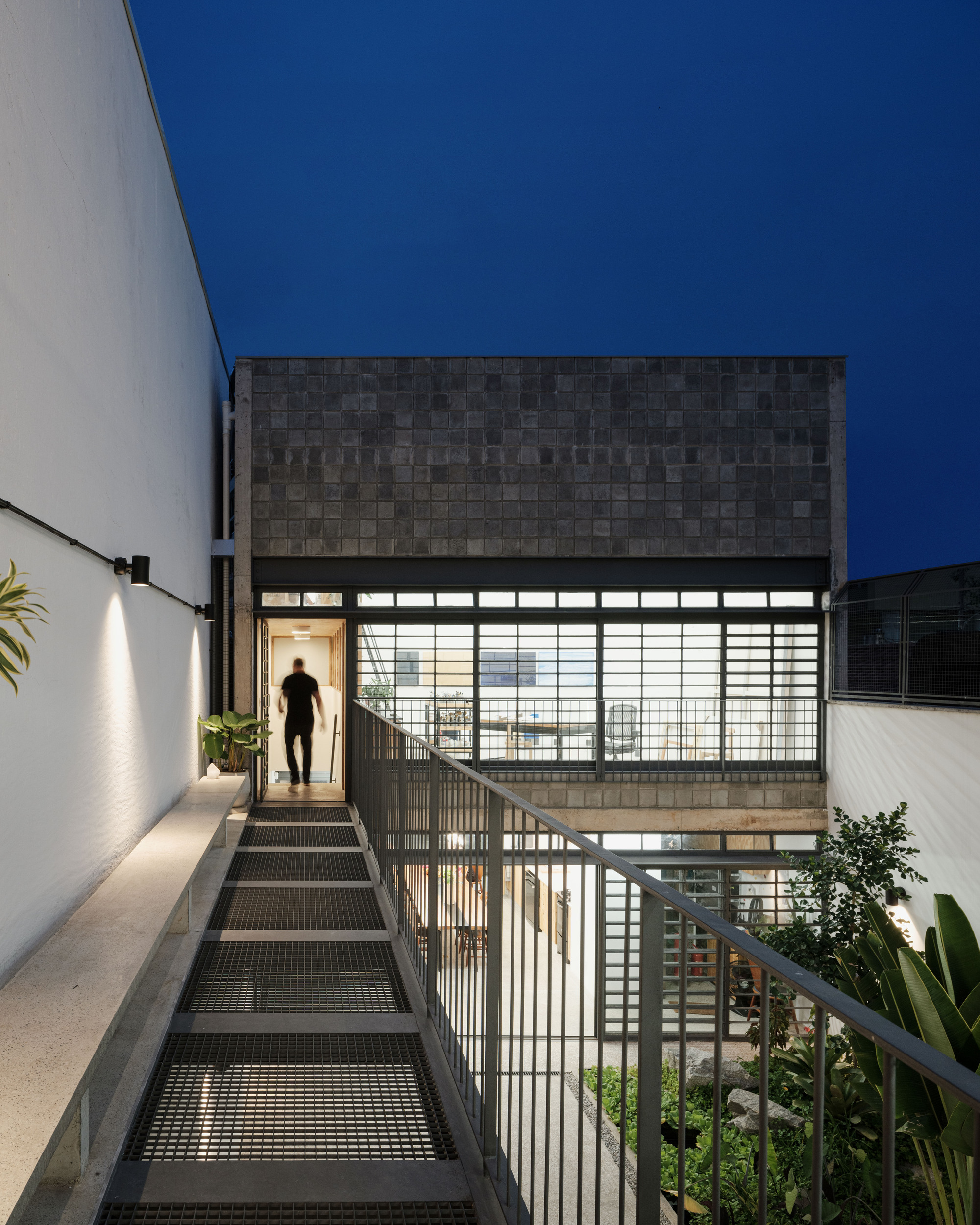 Metal stair leading to the translucent facade with a person ascending at twilight