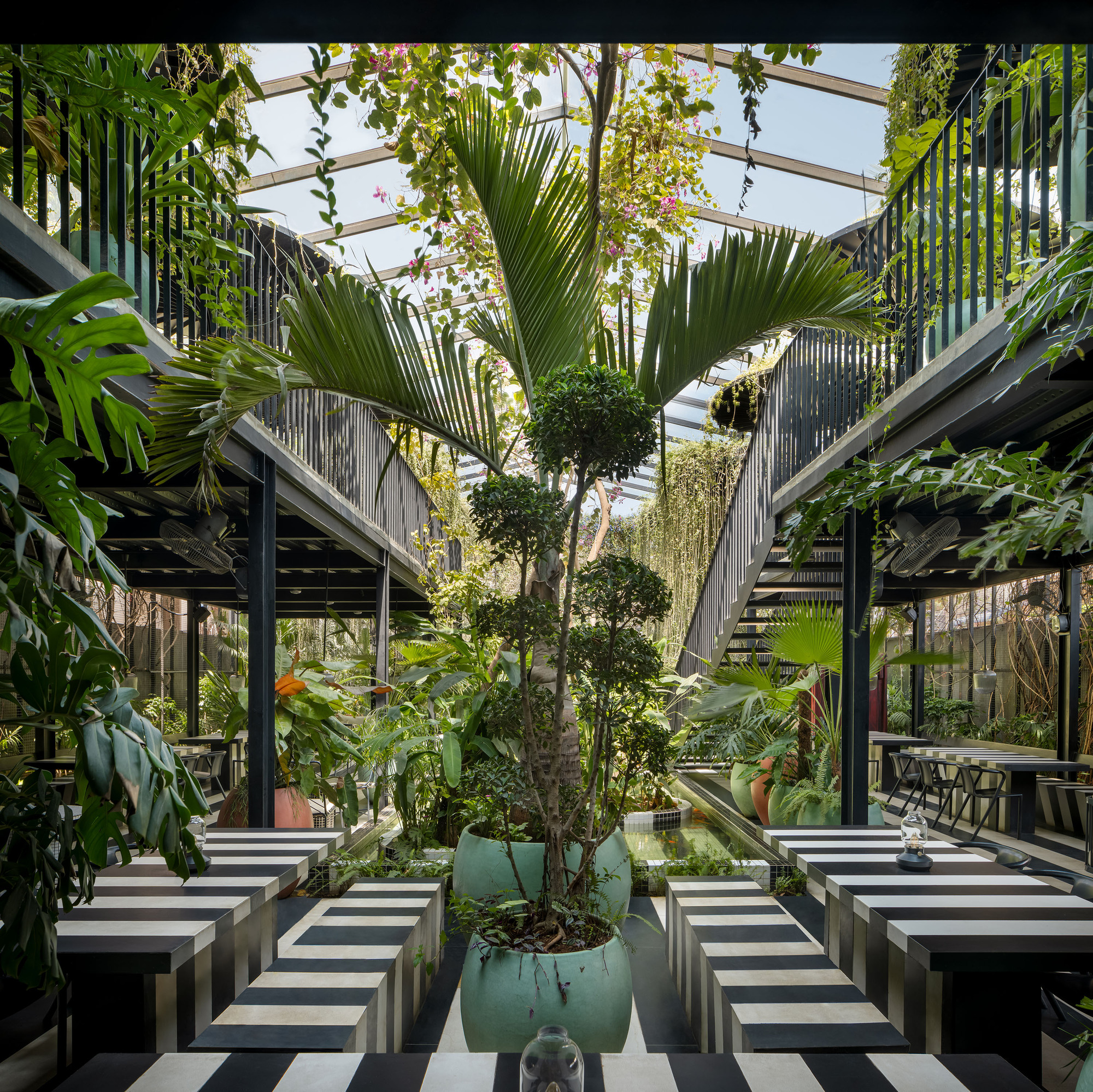 Central courtyard with striped concrete tables flanking potted trees under a glass and steel canopy