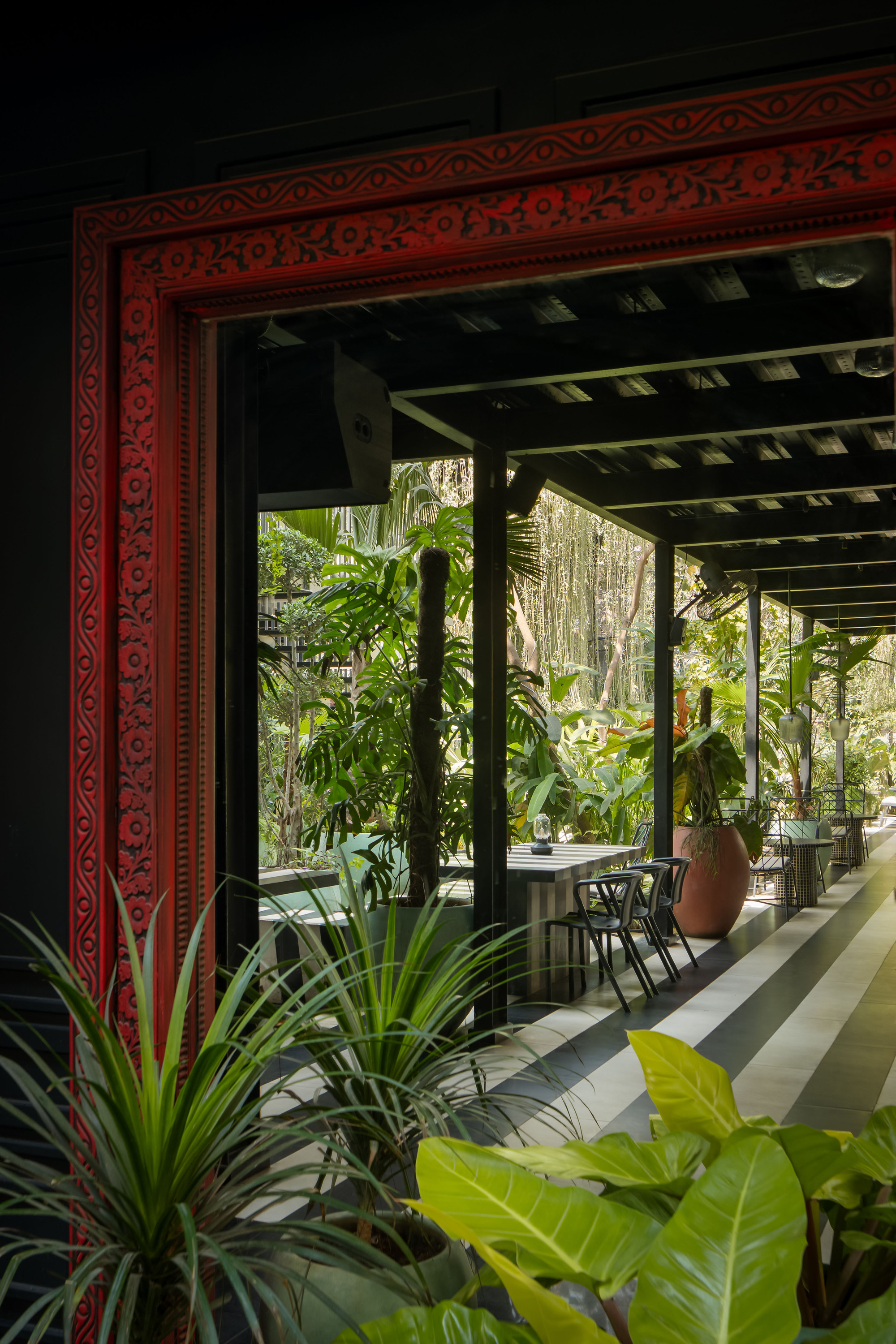 View through a red carved timber doorframe toward the striped floor and garden beyond