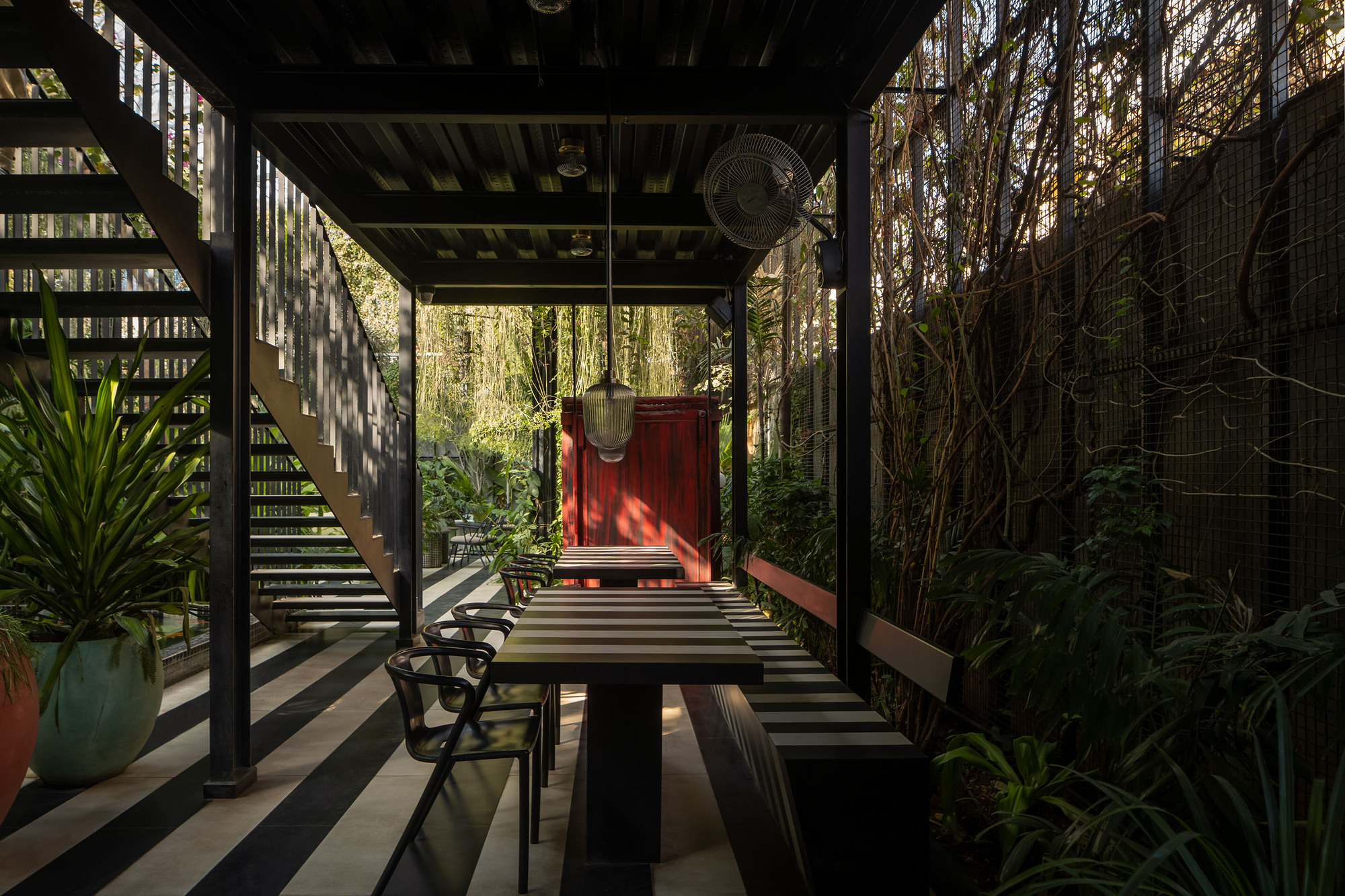 Covered terrace with striped decking and dining table looking toward the red portal in afternoon light