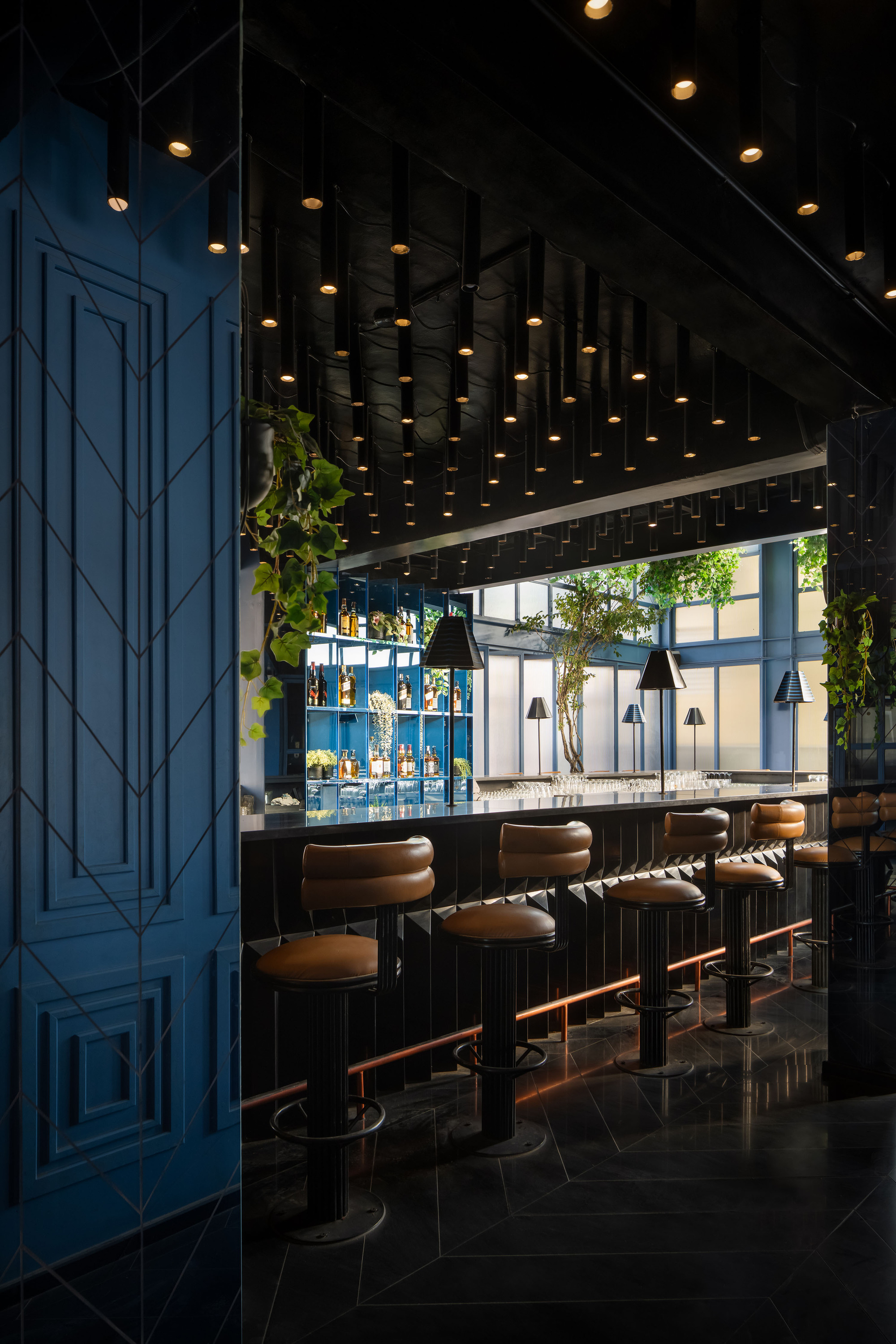 Bar interior with black ceiling grid of pendant lights and blue paneled wall at left