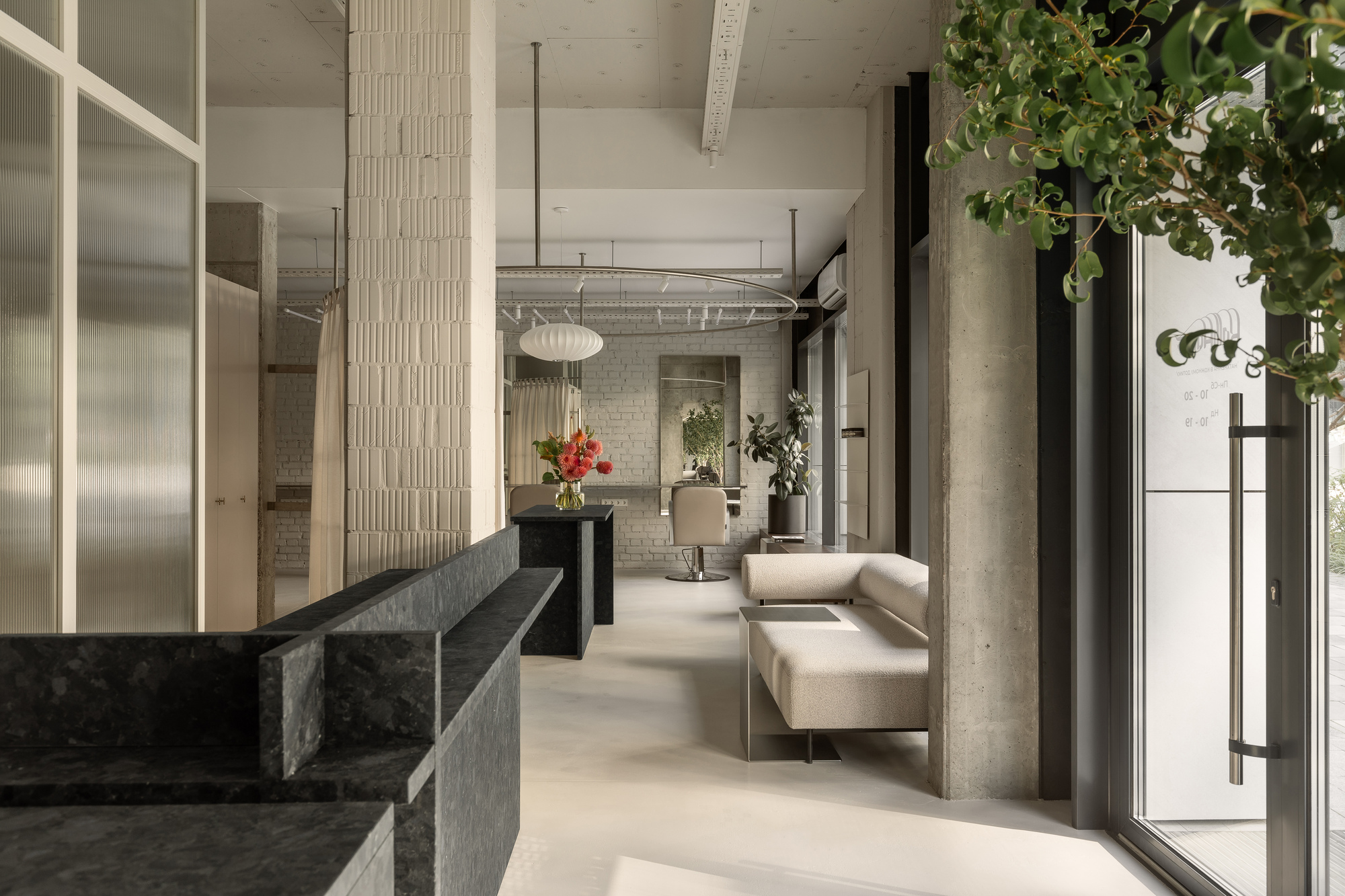 Open interior with dark stone reception counter, exposed concrete columns, and potted greenery near glazed entrance