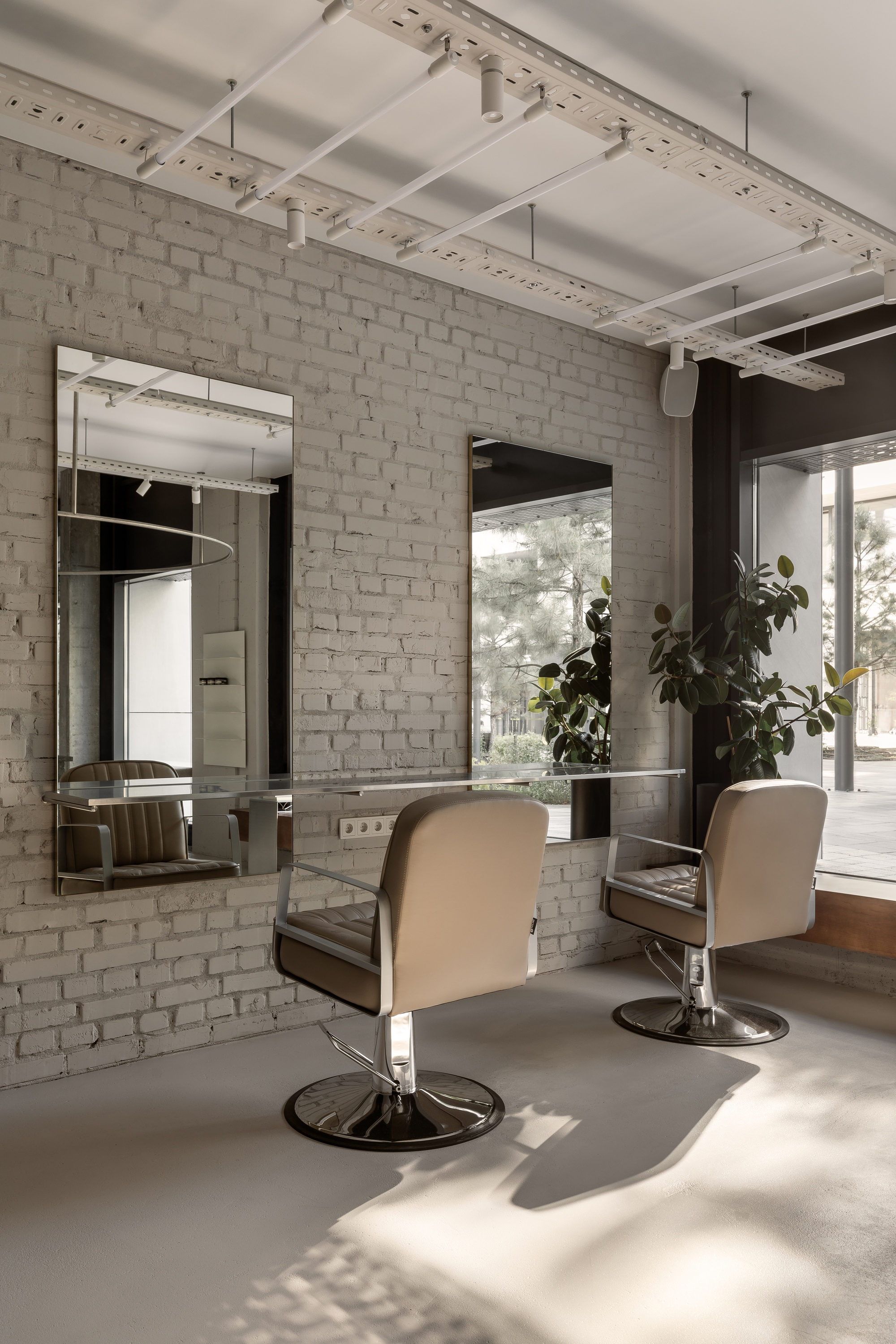 Salon area with white-painted brick wall, framed mirrors, styling chairs, and sunlight filtering through glass