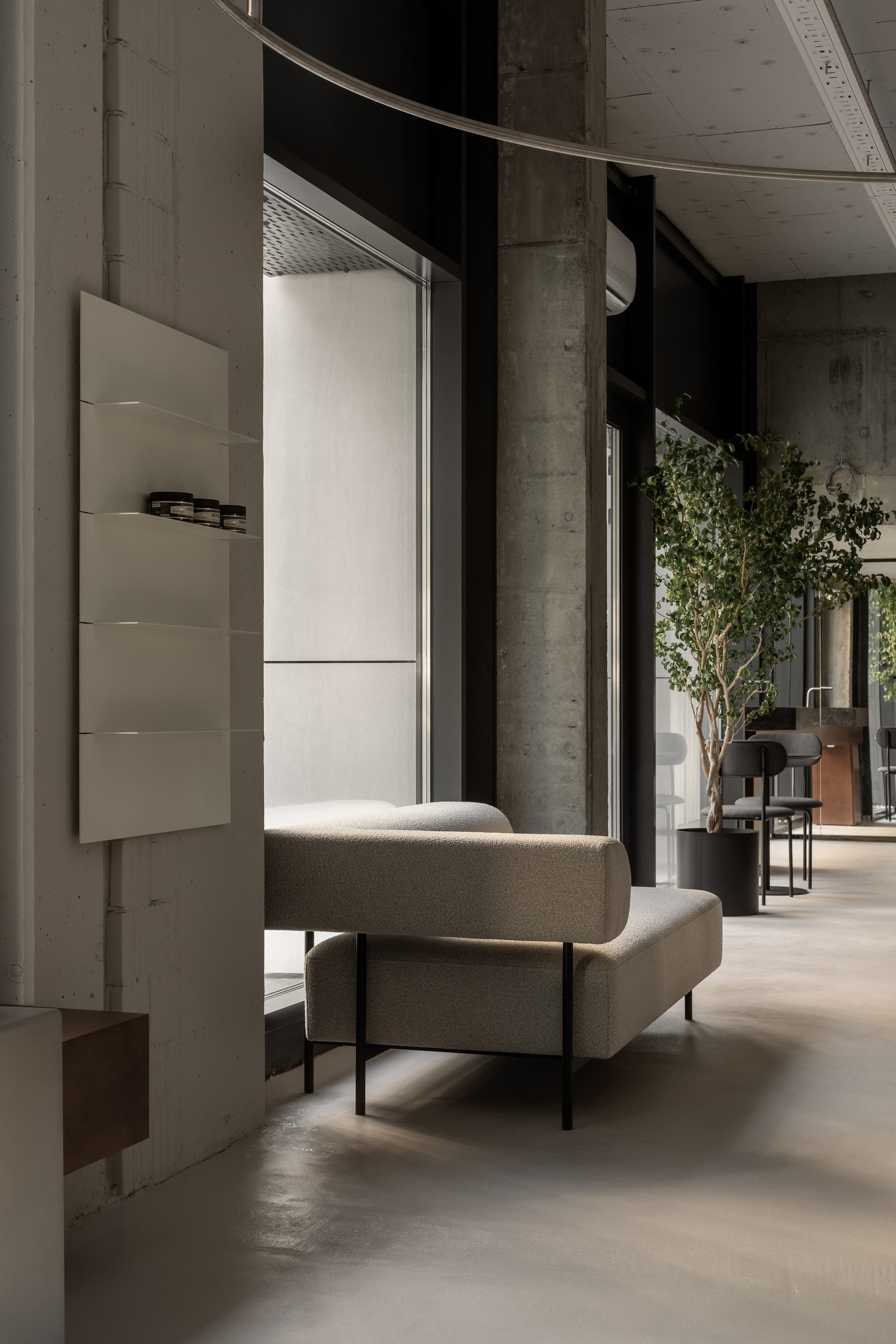 Seating alcove with concrete columns, floating display cabinet, curved metal track, and view toward planted areas