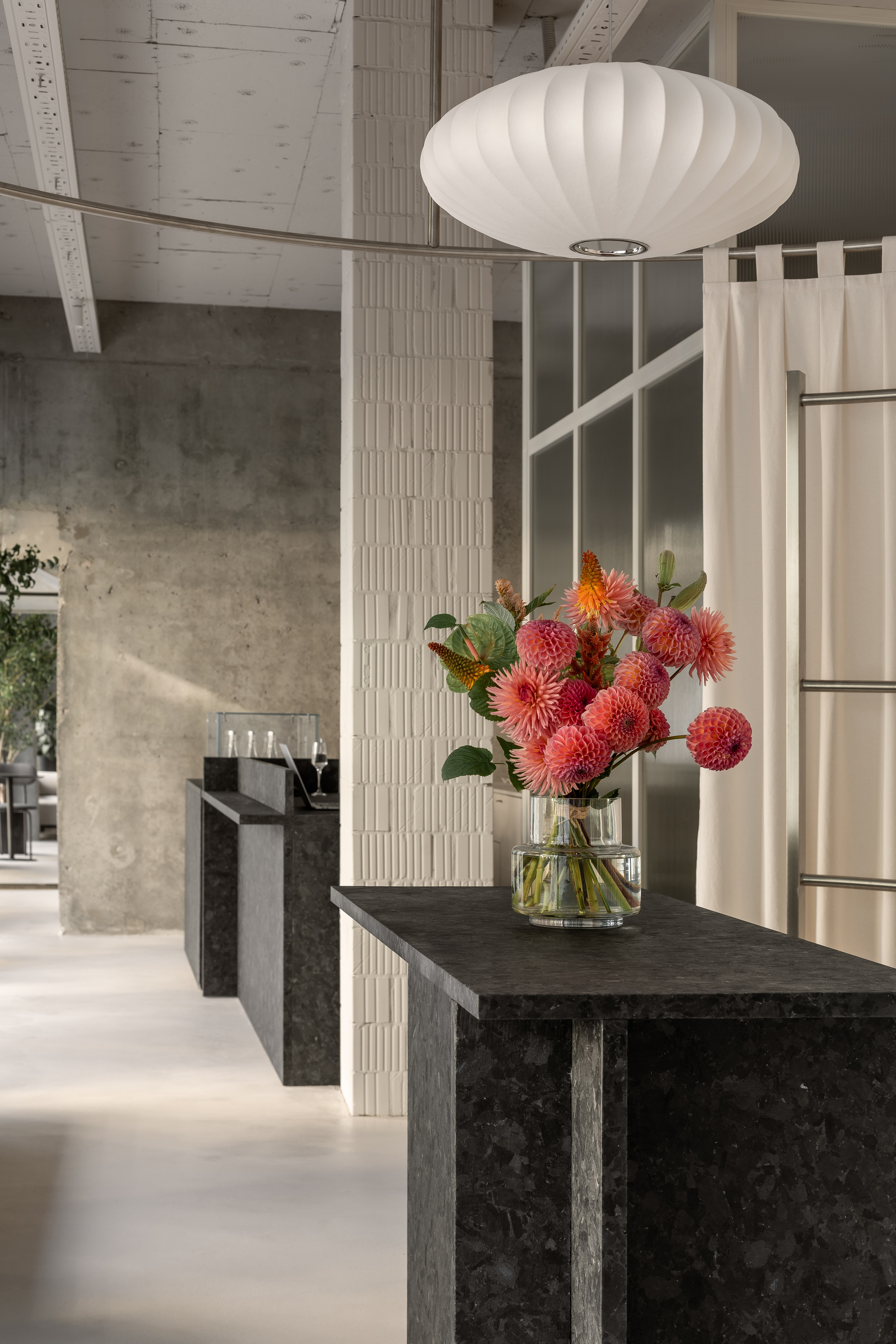 Interior view of dark stone counter with red protea flowers beneath a ribbed pendant light