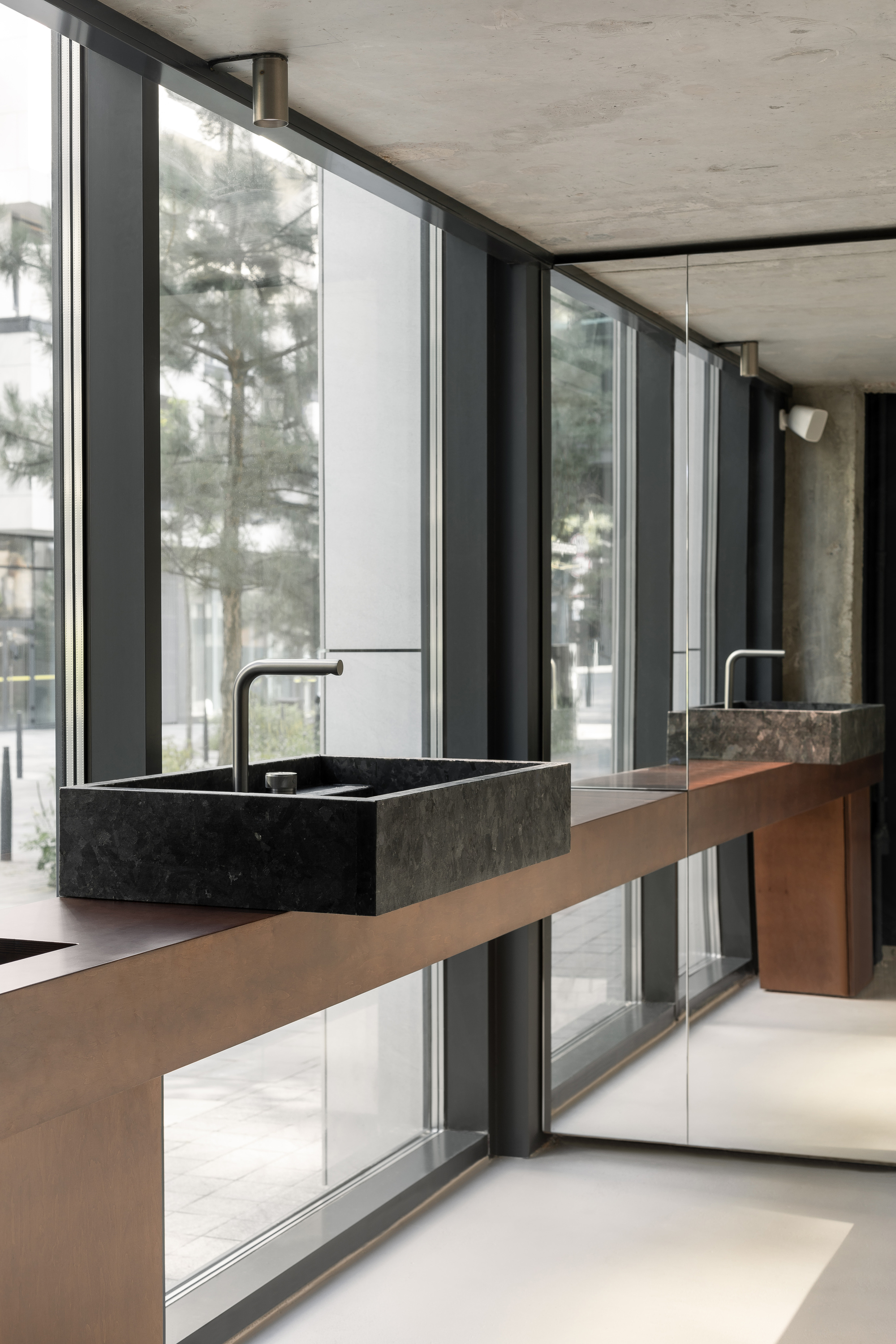 Cantilevered timber vanity with dark stone basin overlooking winter trees through floor-to-ceiling glazing