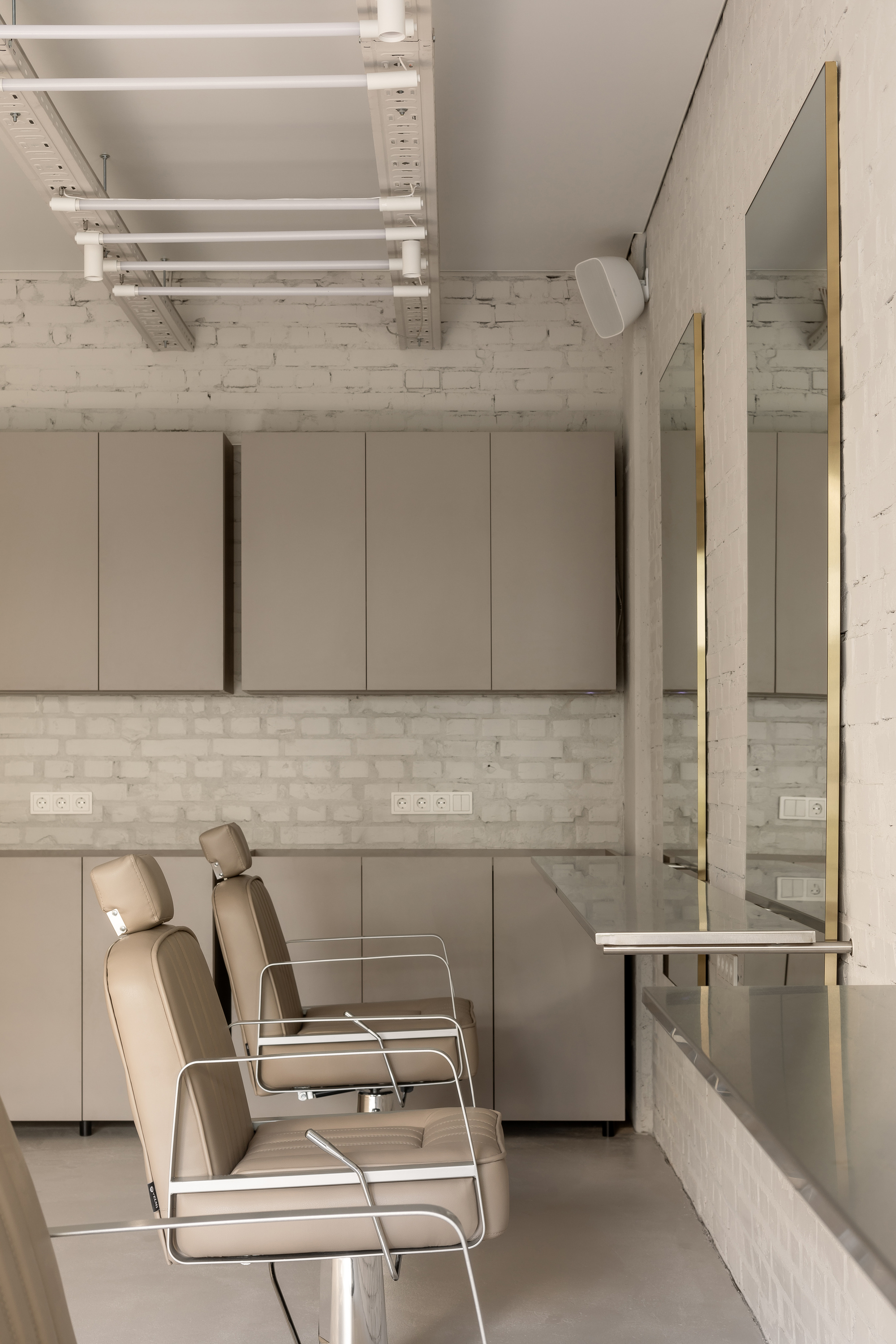 Salon chairs against white brick wall beneath exposed ceiling joists and wall-mounted cabinets