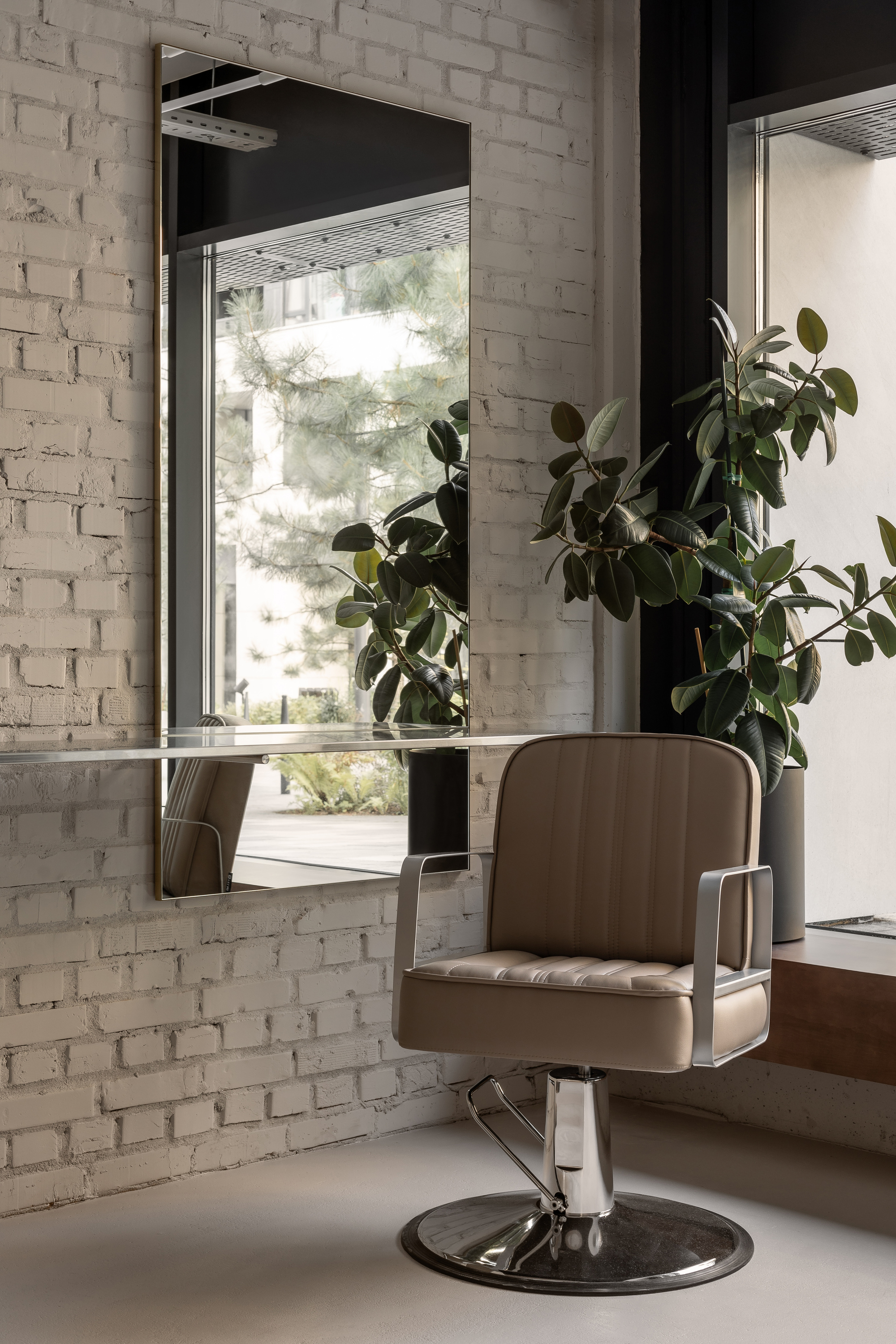 Salon chair reflected in mirror beside window with potted plants on timber ledge