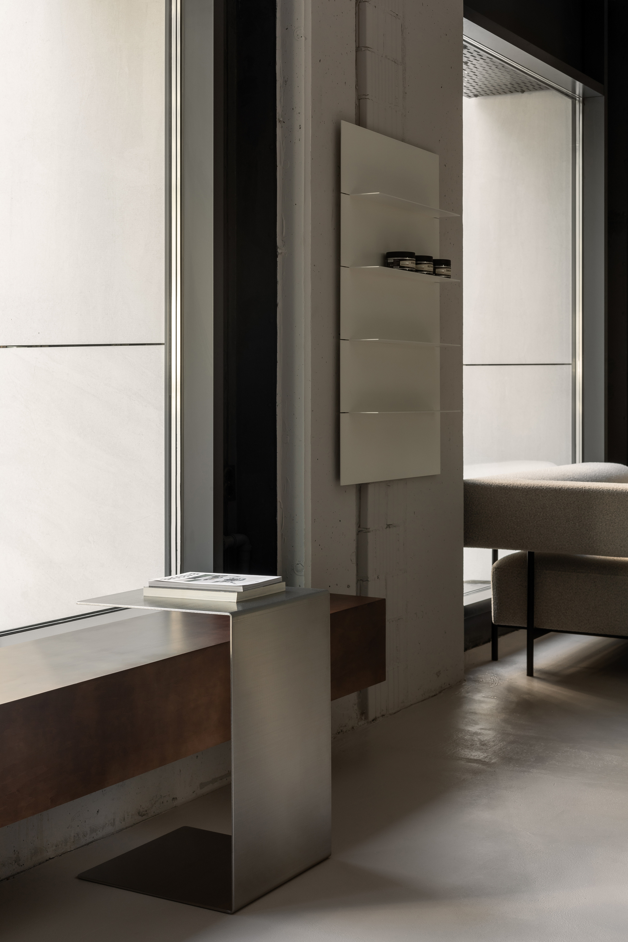Brushed metal pedestal table beside concrete wall and full-height glazing with soft natural light