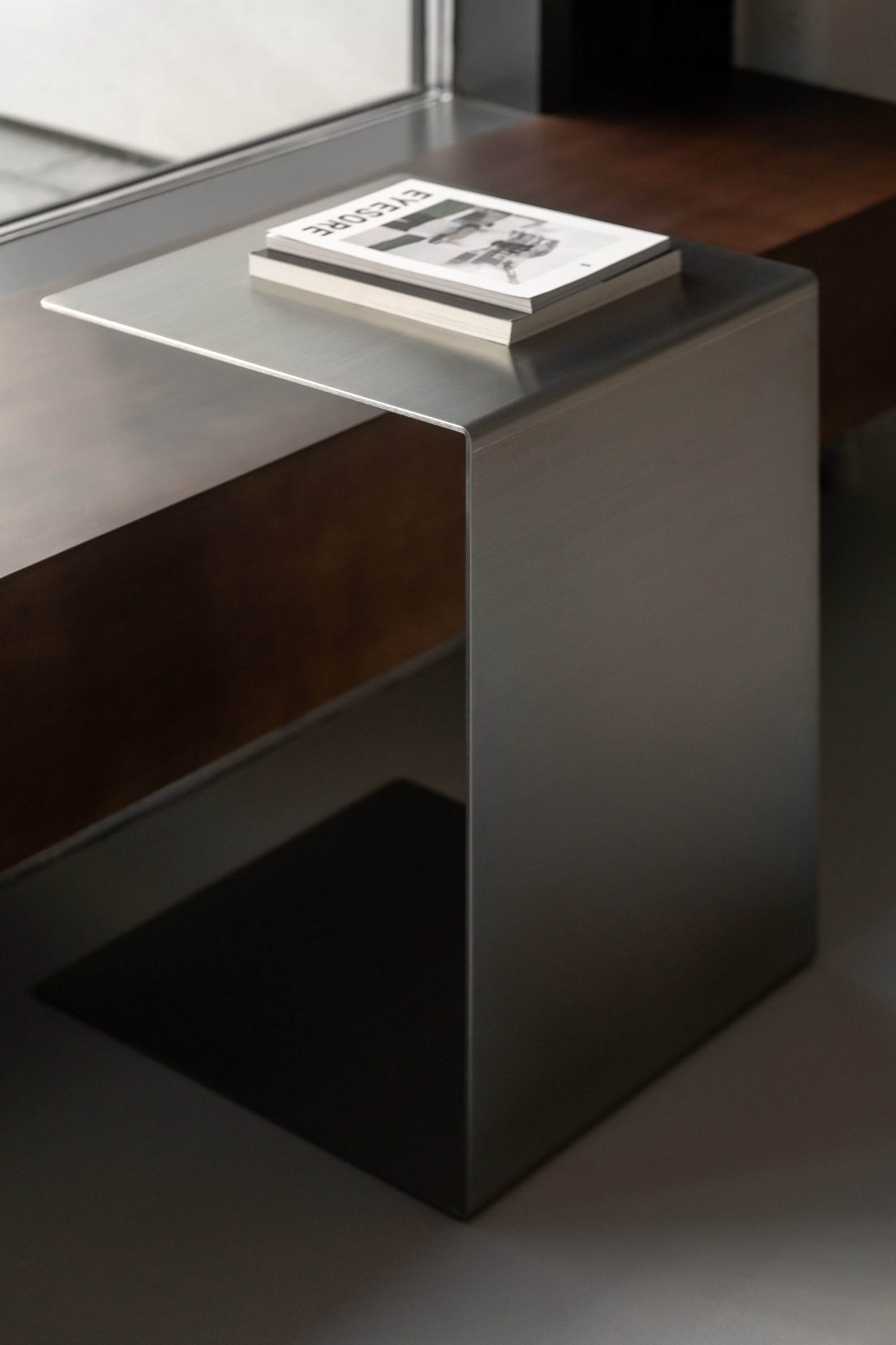 Close-up of brushed stainless steel side table with a book resting on its cantilevered top