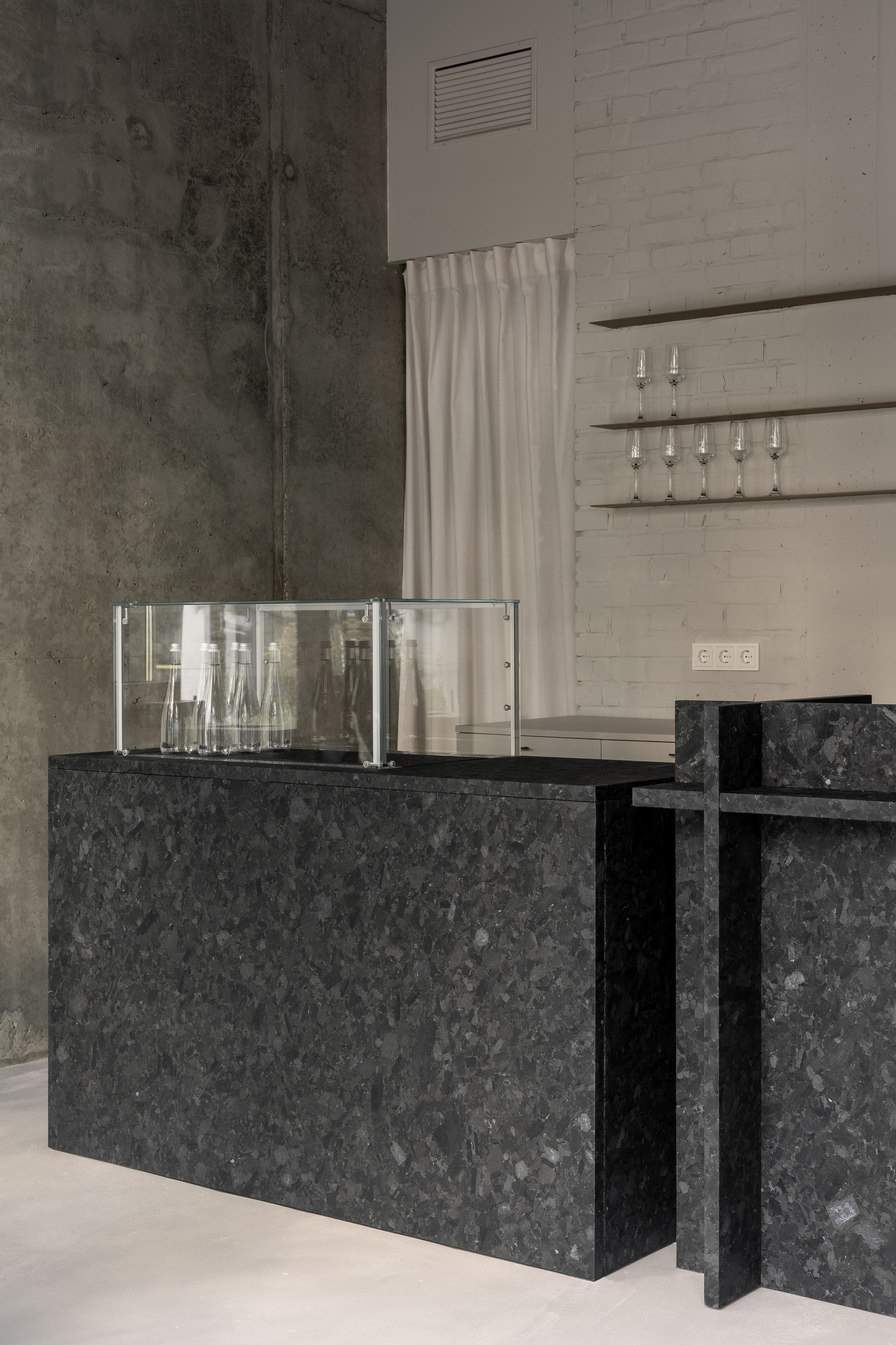 Reception counter in dark speckled stone with glass display box and concrete walls behind white curtain