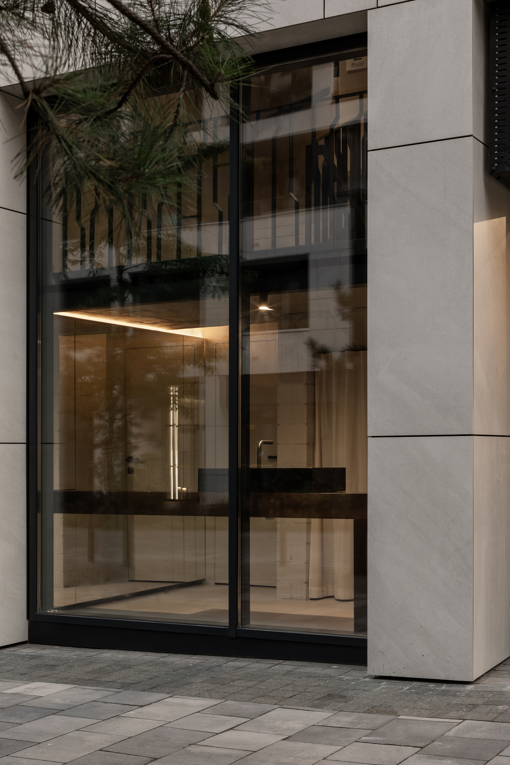 Street view through glazed storefront with black frames showing illuminated interior counter at dusk