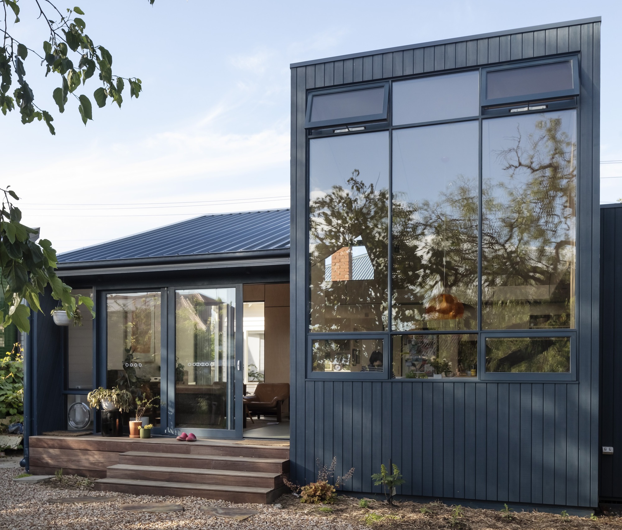 Two-volume residence with vertical metal cladding and tall glazing beside timber entry steps and gravel courtyard