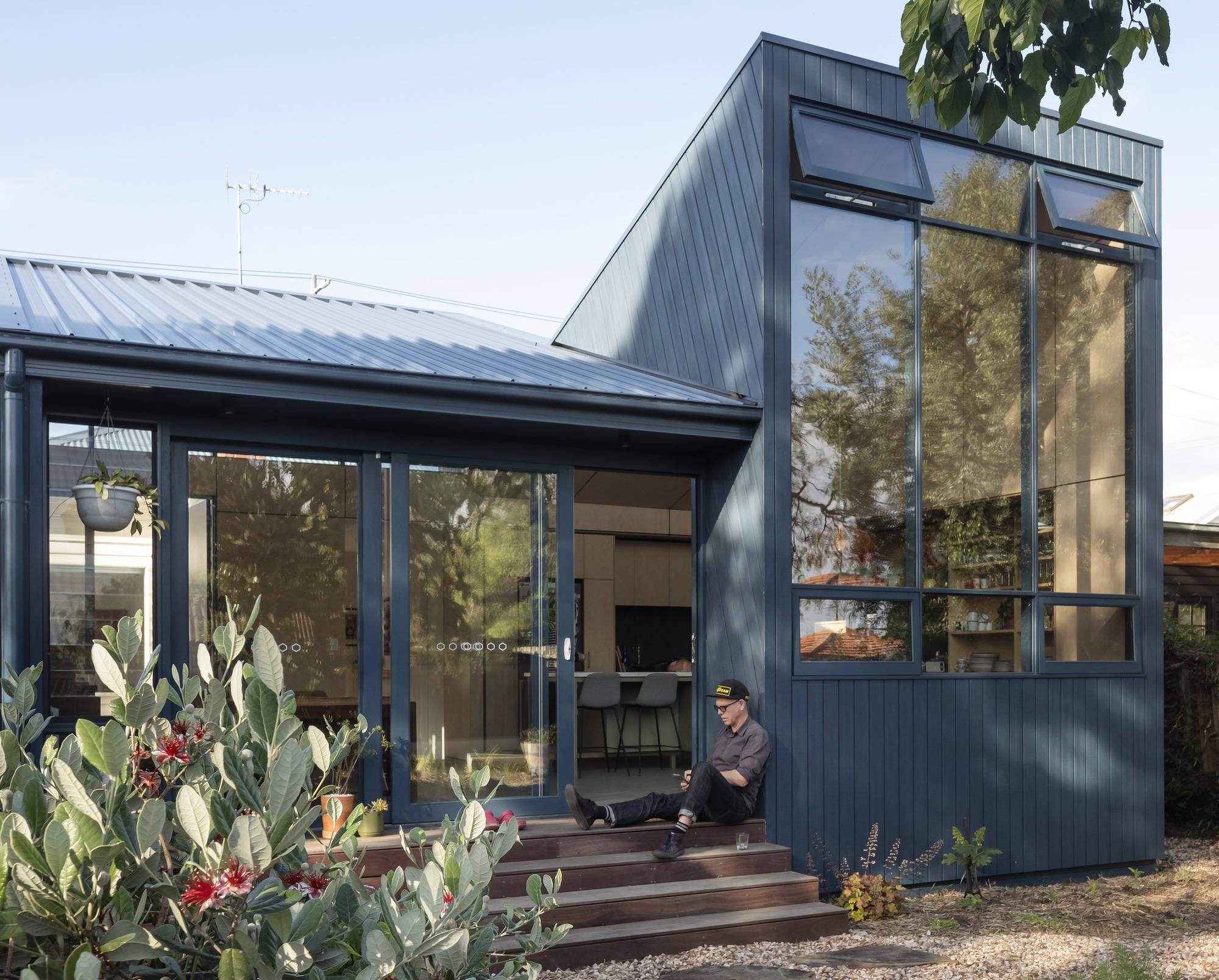 Entrance view showing timber steps leading to glass doors with a resident sitting on the threshold