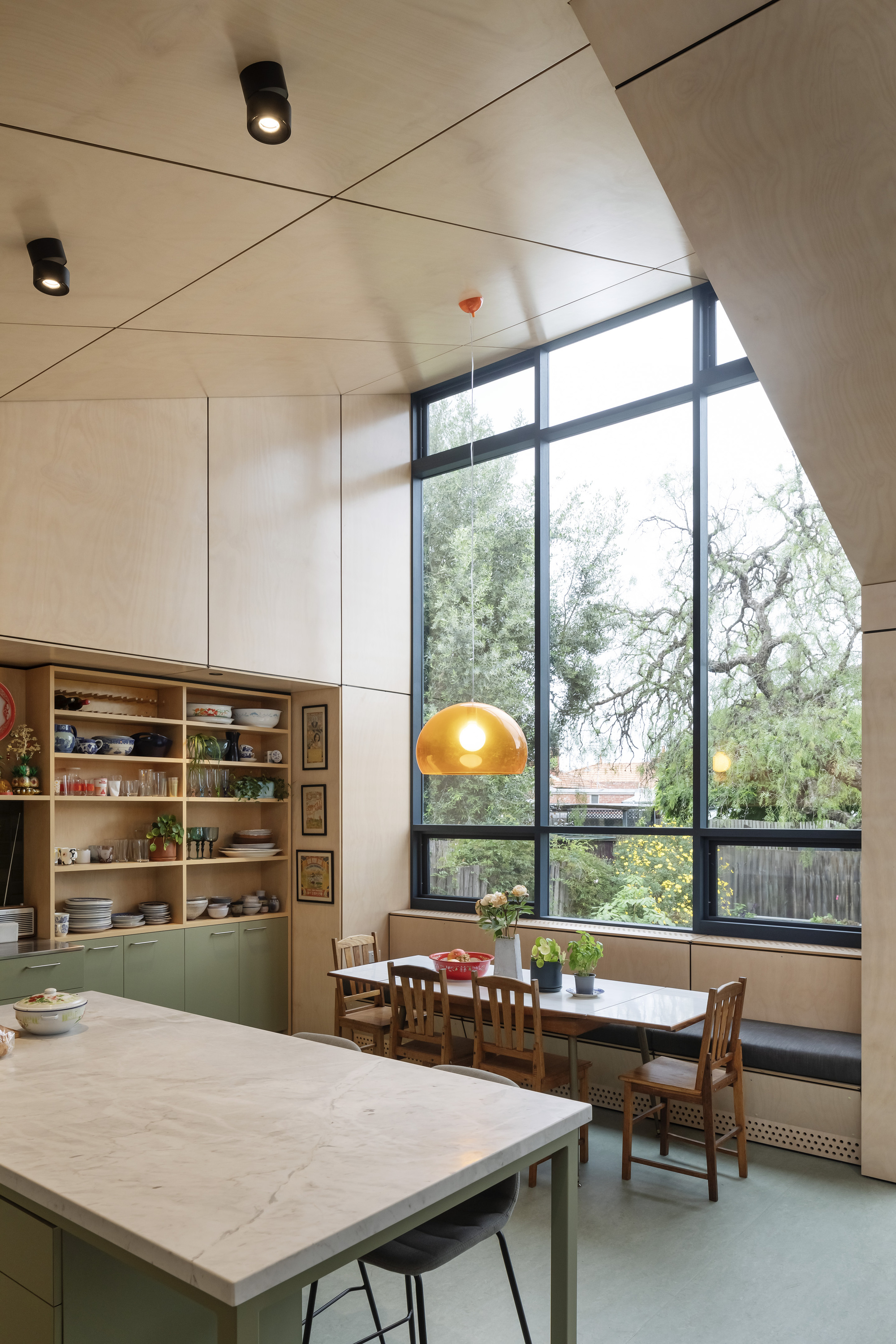 Double-height dining space with tall windows framing tree views and amber pendant light overhead