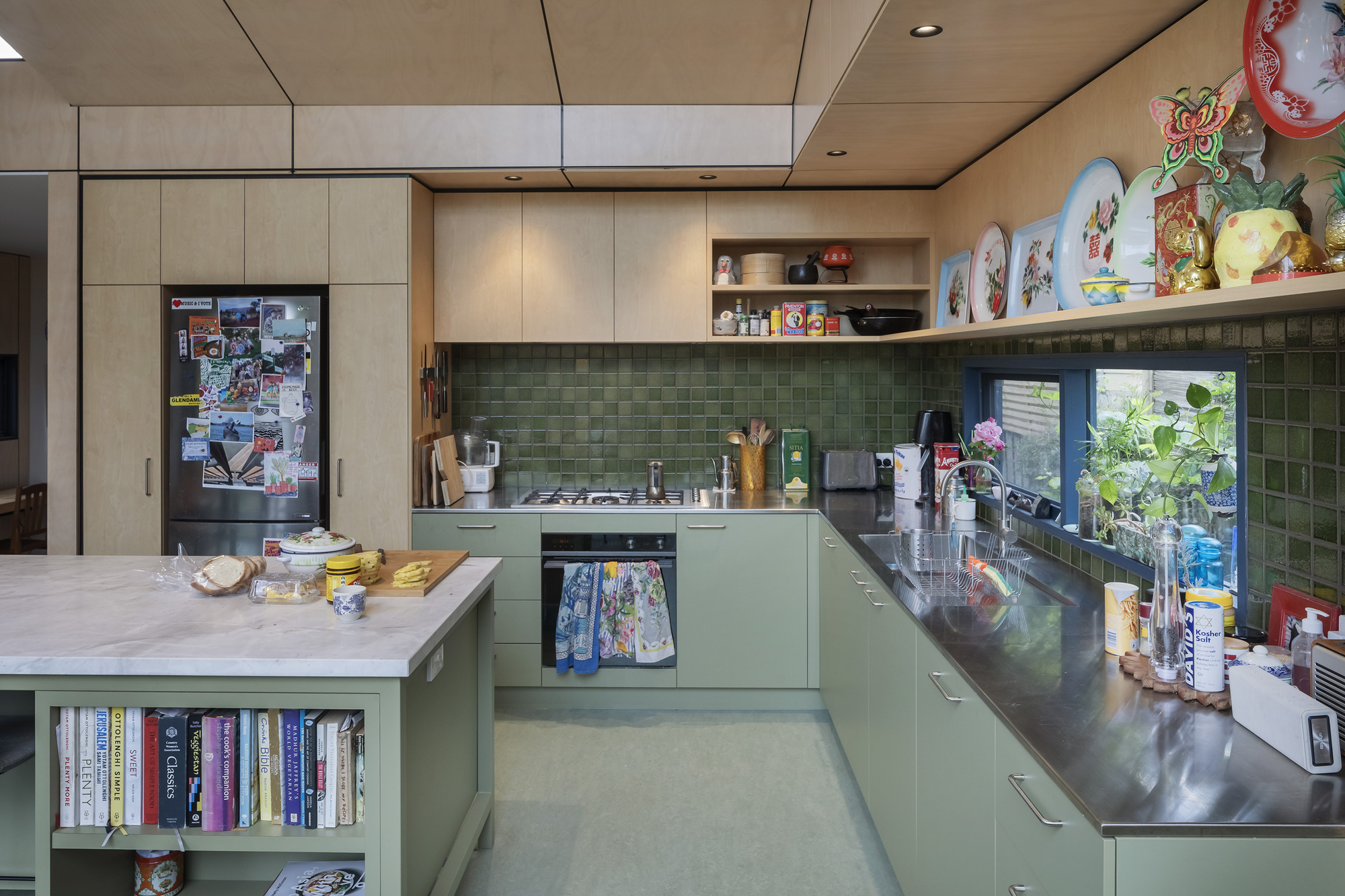 This image showcases a modern kitchen with a unique blend of materials and colors. The kitchen features green cabinets, a stainless steel countertop, and a plyw