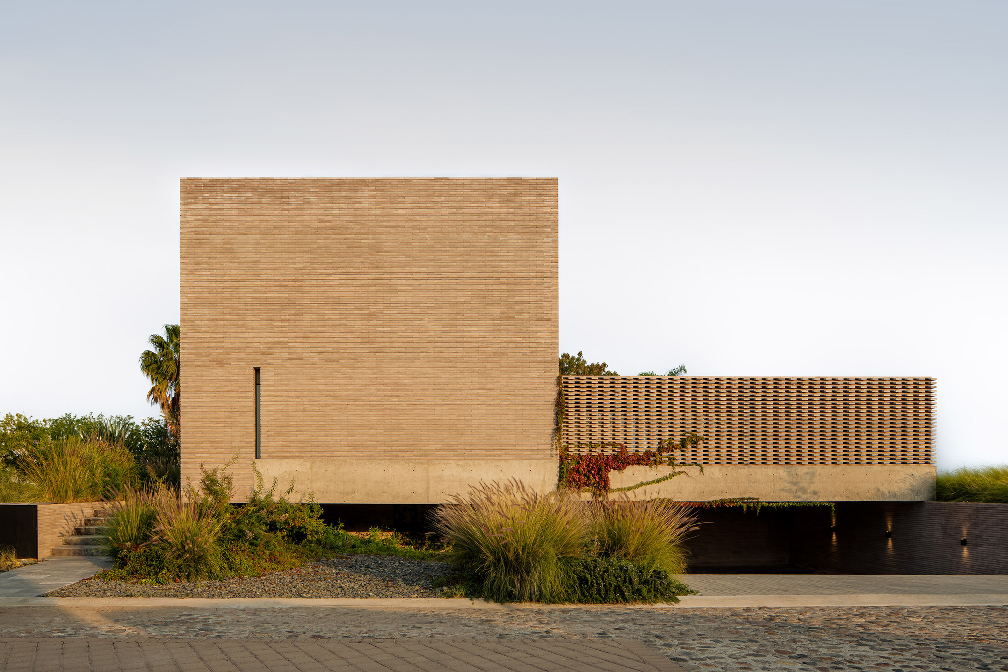Street facade with horizontal brick coursing and perforated screen wall flanked by native grasses