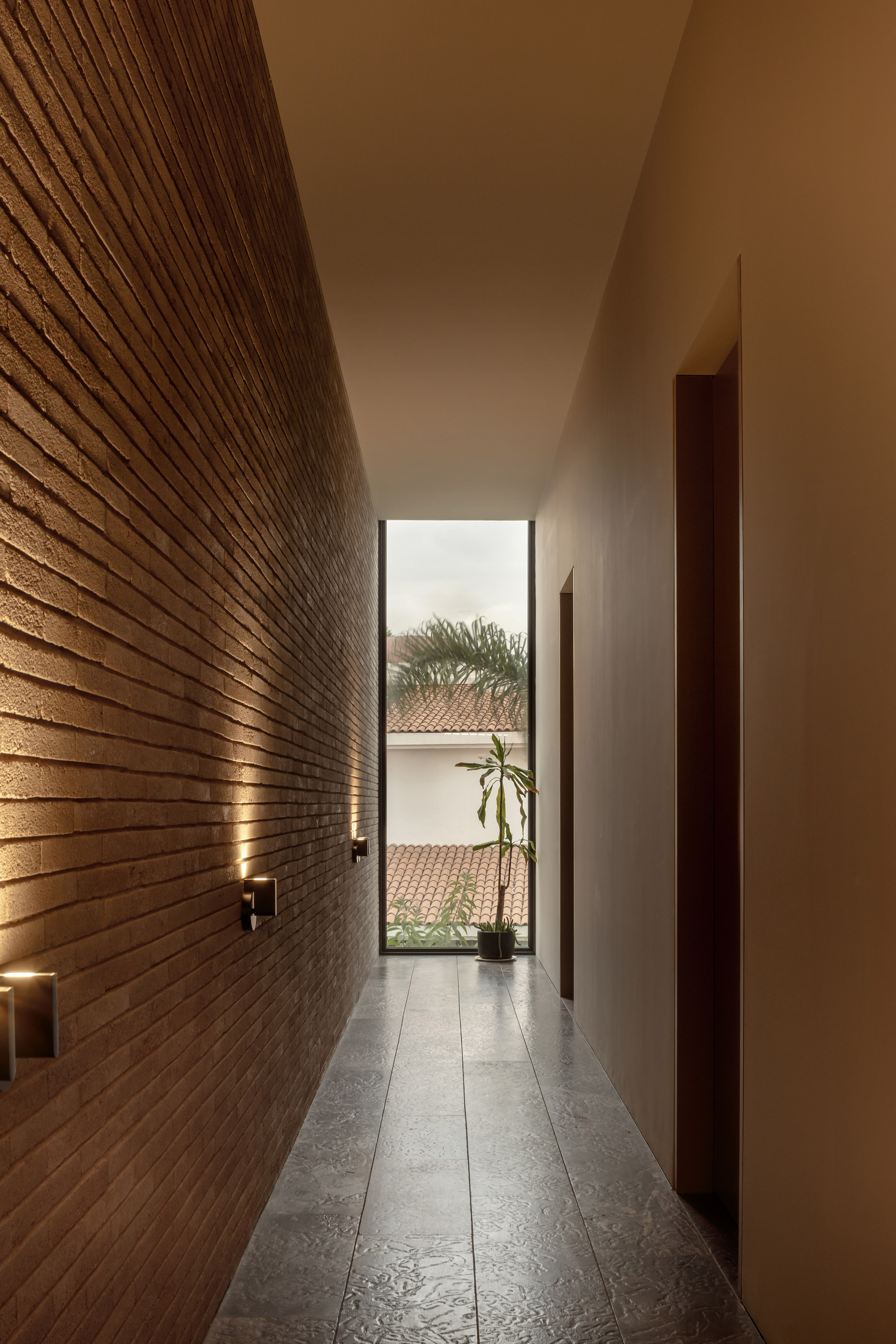 Narrow corridor with horizontal timber slat wall and narrow window framing a planted courtyard
