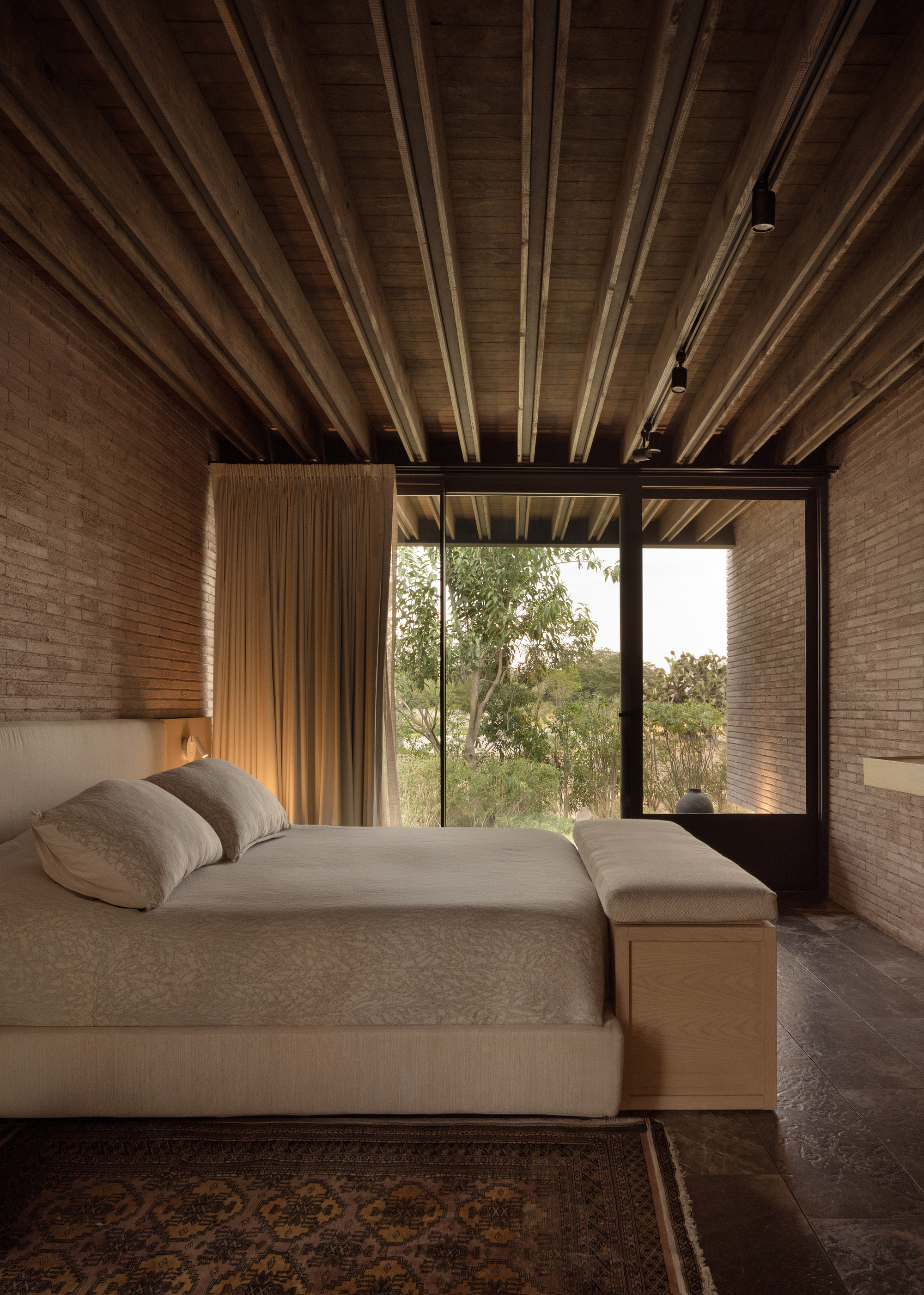 Bedroom with exposed timber beam ceiling and corner window opening to surrounding trees