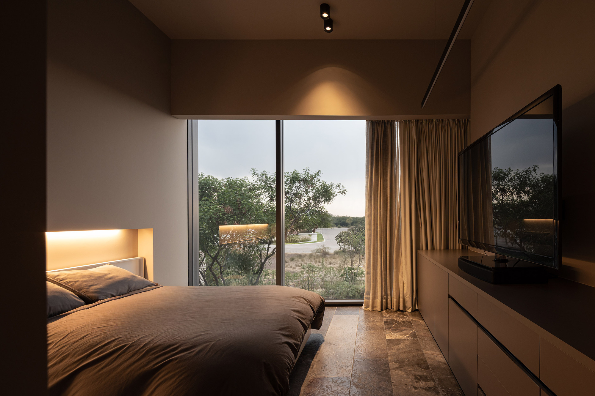 Bedroom with floor-to-ceiling glazing overlooking arid landscape at dusk