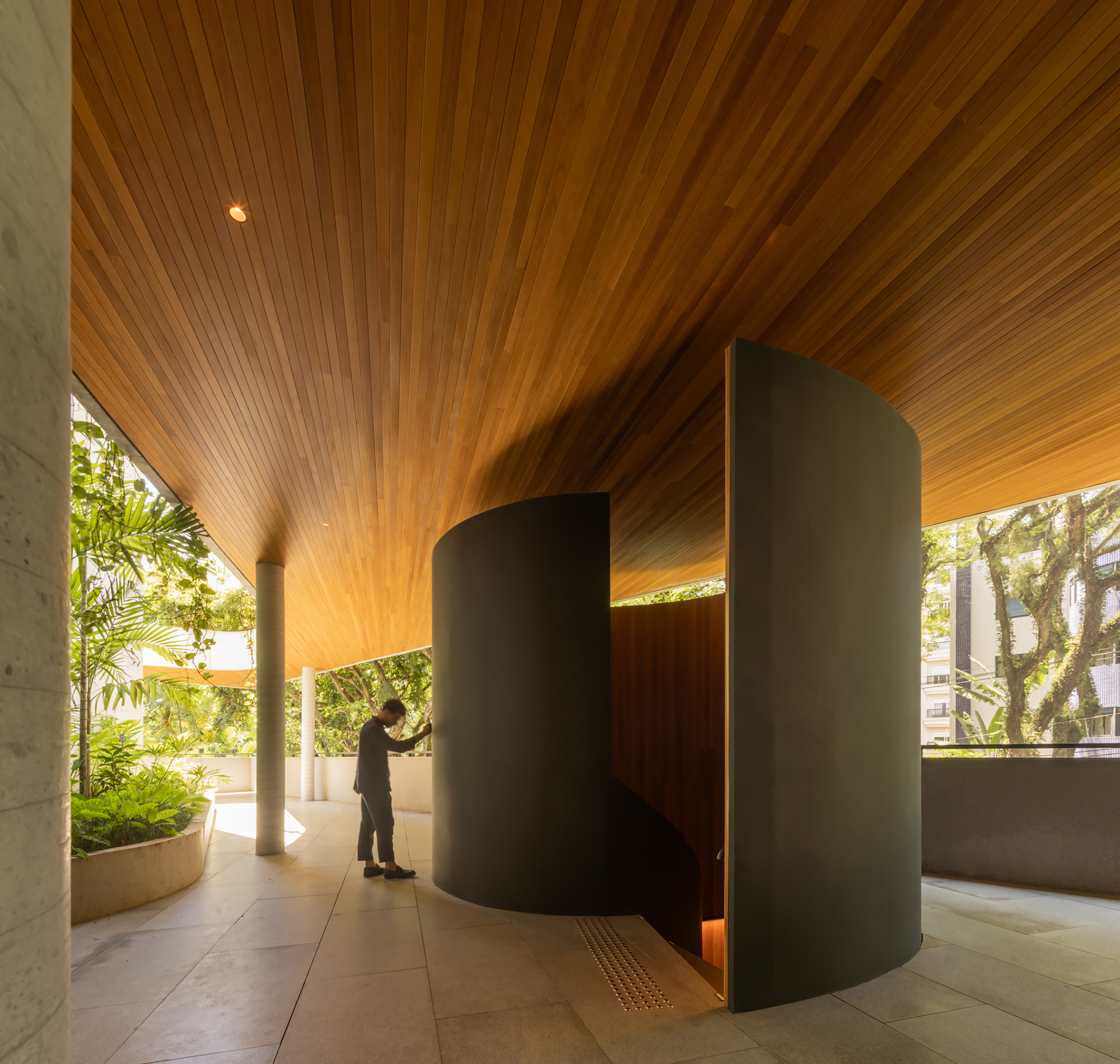 Covered entry lobby with timber slat ceiling and cylindrical partition as a figure approaches