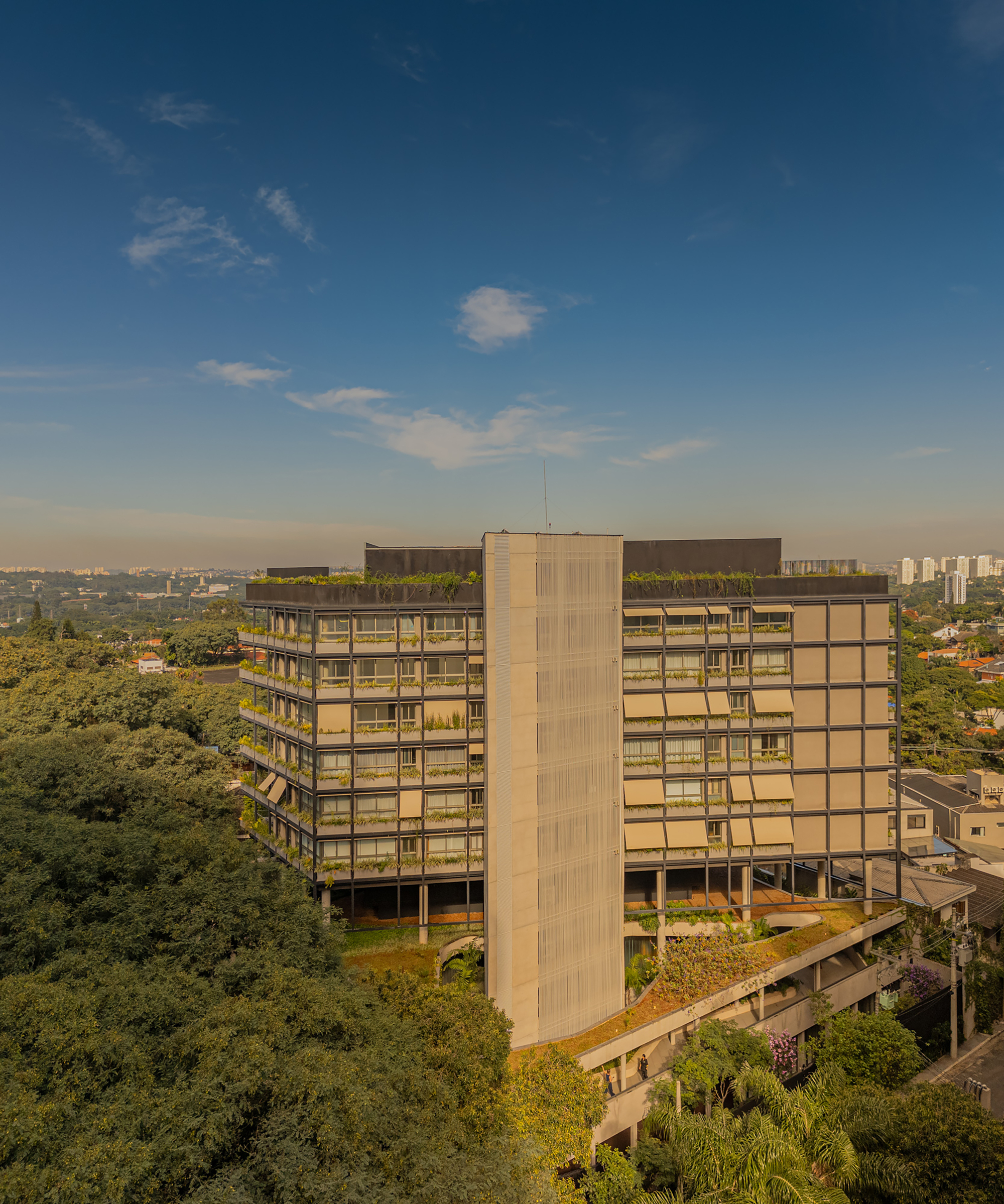 Aerial view of the multistory residential block with planted balconies surrounded by dense tree canopy