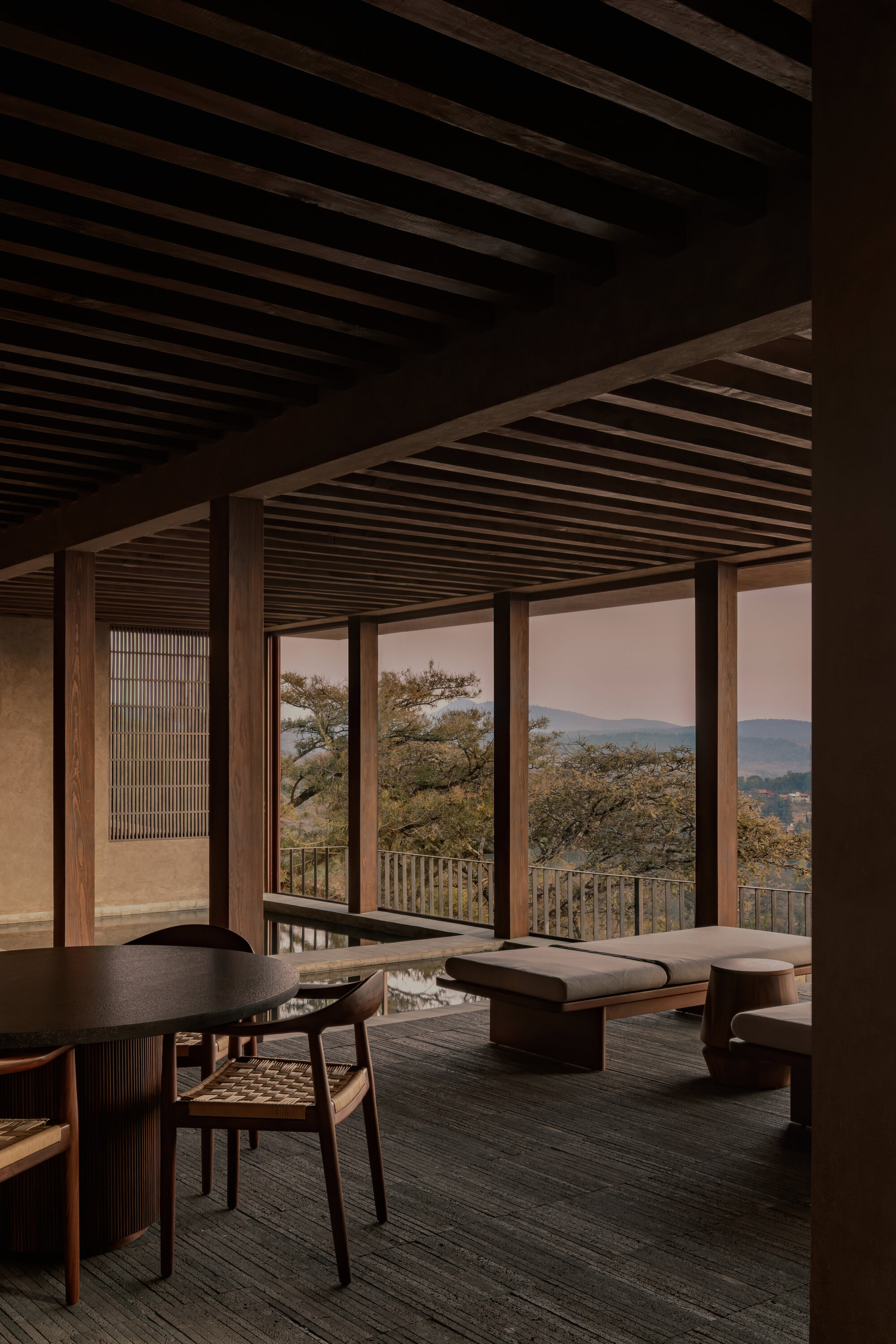 Interior living space with exposed timber ceiling beams and sliding glass doors opening to mountain views at dusk