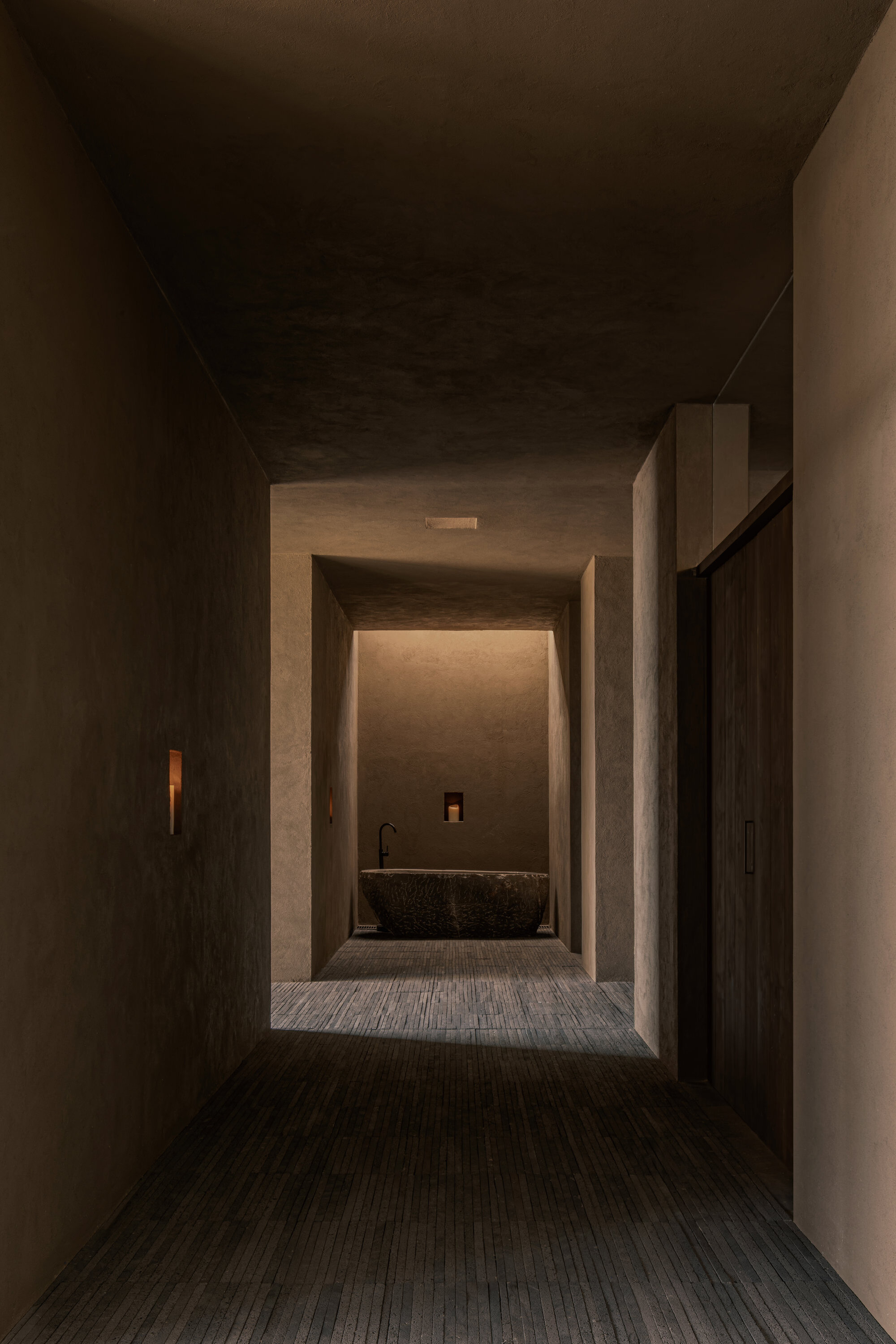 Layered concrete threshold spaces framing a stone basin under concealed ceiling lighting