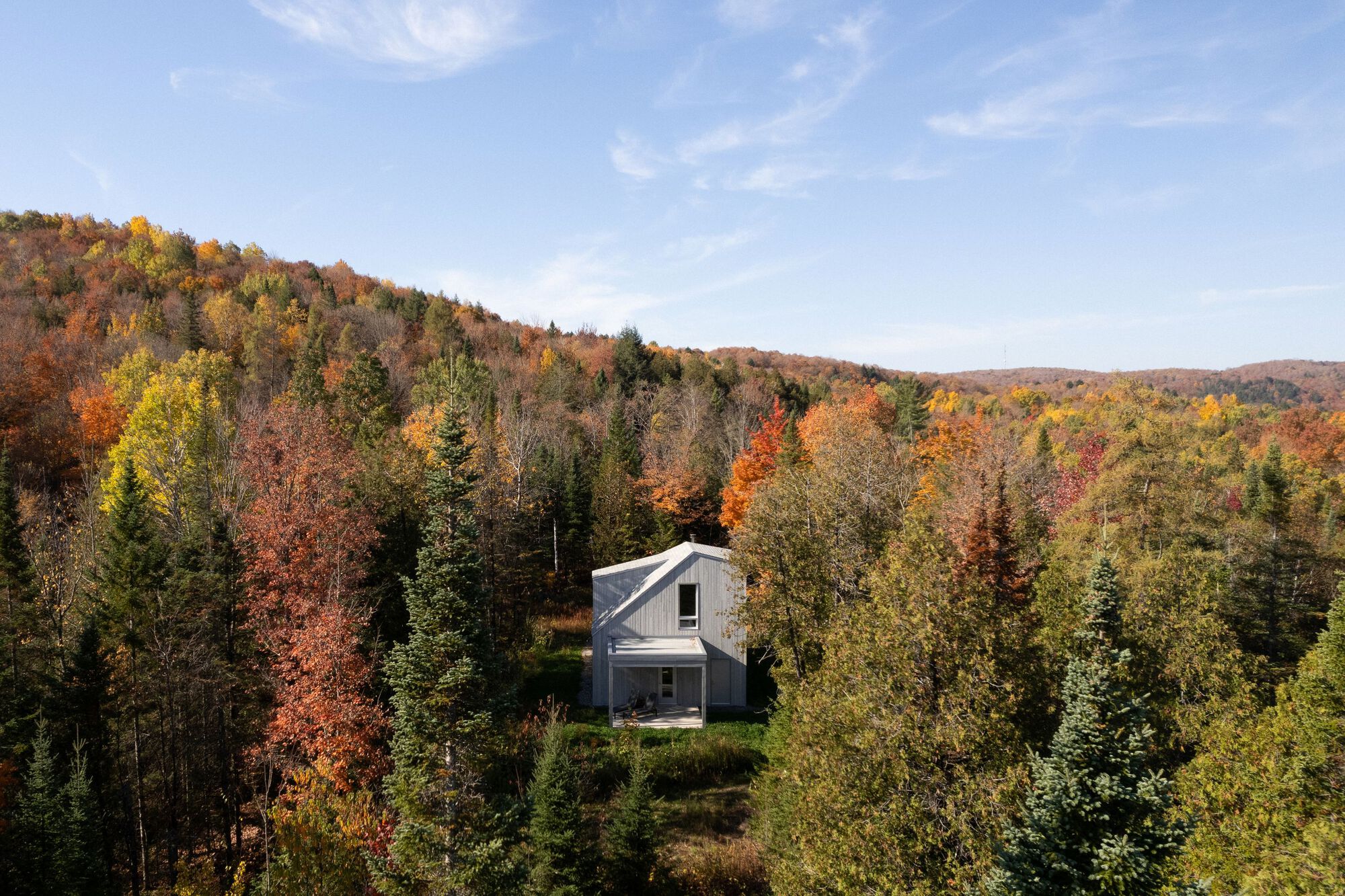 The house nestled in a clearing among mixed forest with fall foliage