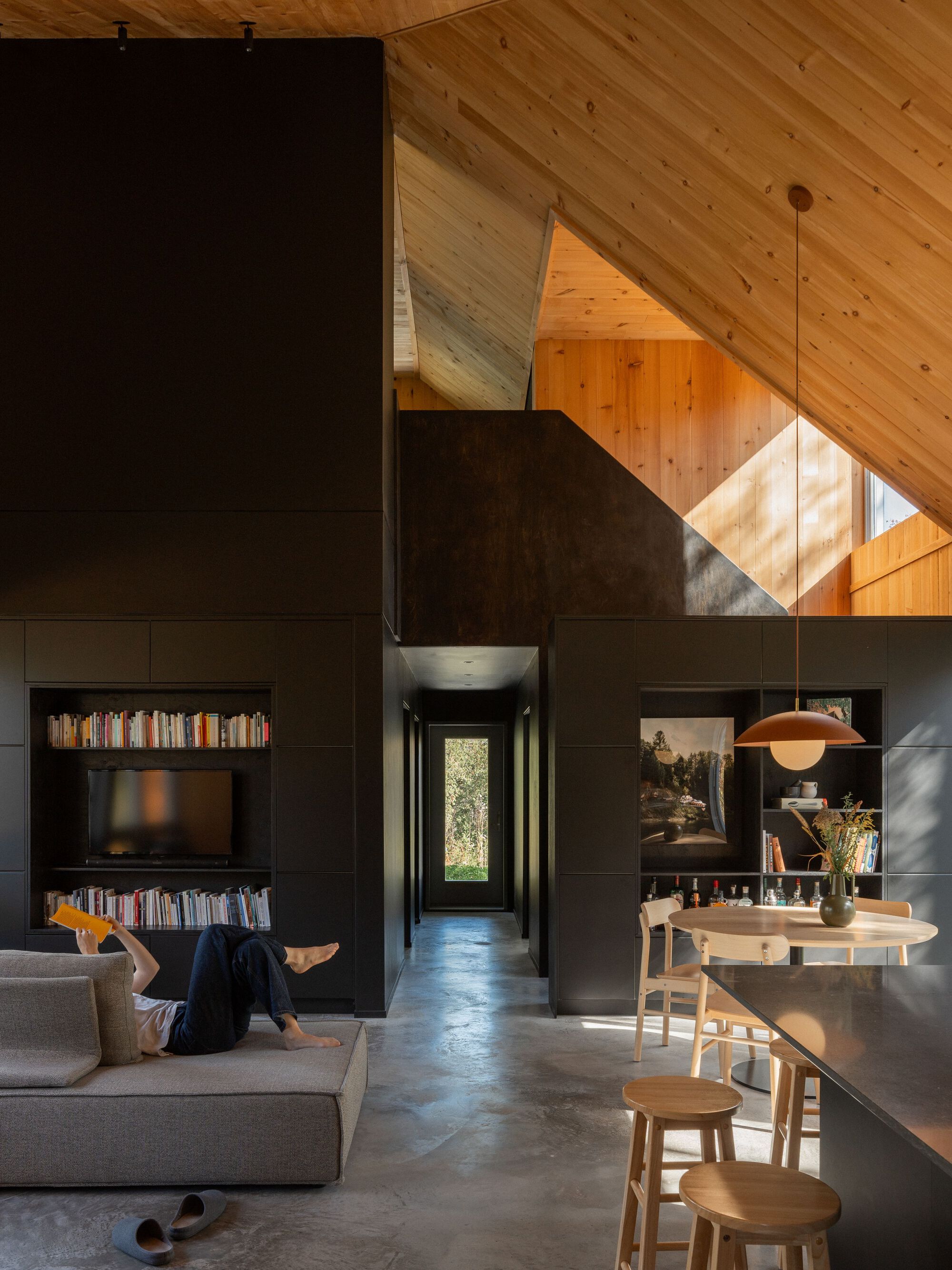 Open interior showing black storage volume under sloped pine ceiling with skylight above dining table