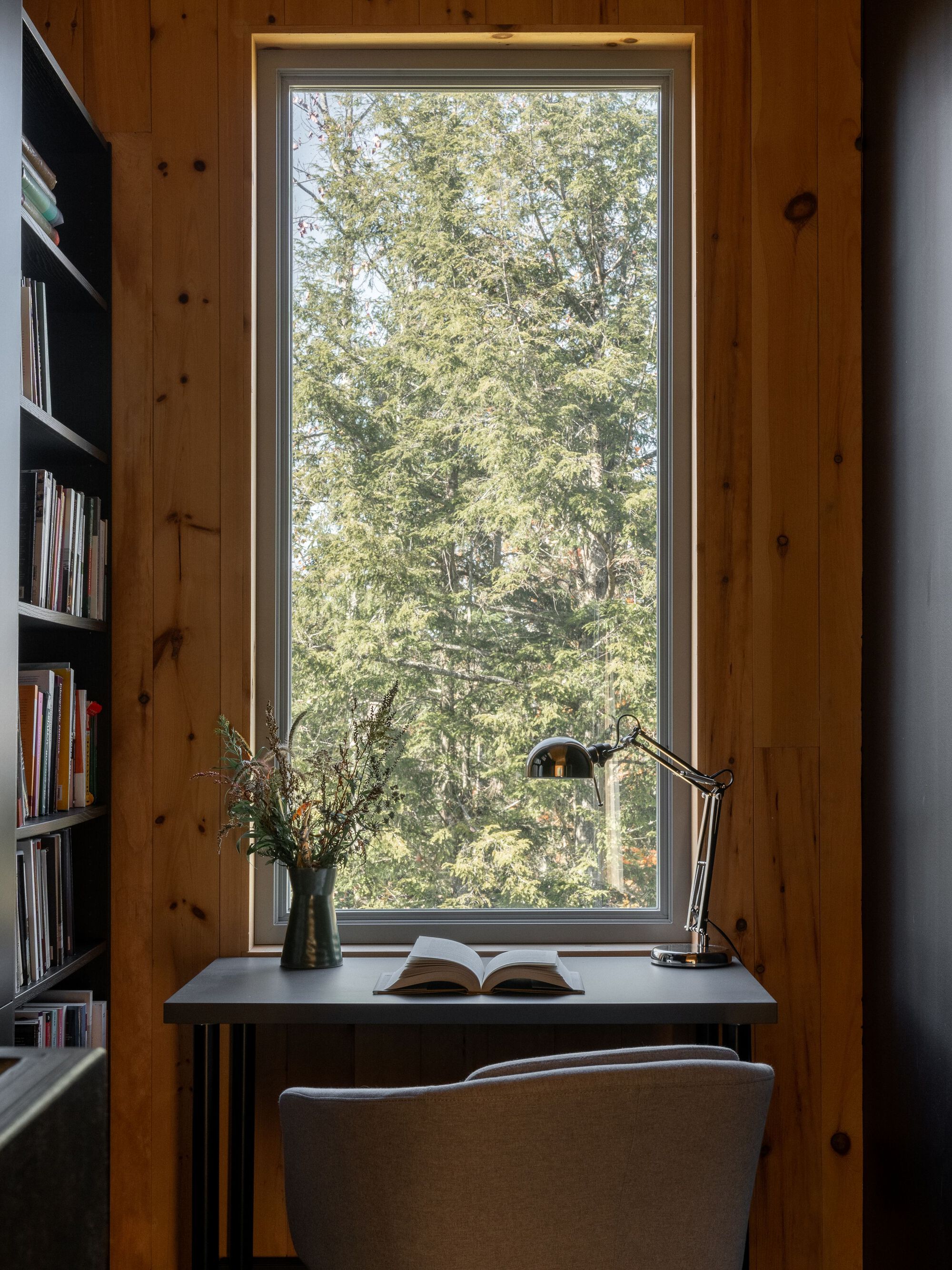 Reading nook framed by knotted pine walls with a tall window overlooking deciduous trees