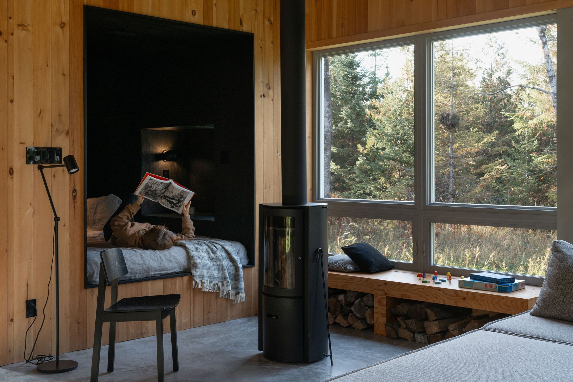 Reading nook with freestanding wood stove and large windows overlooking forested landscape
