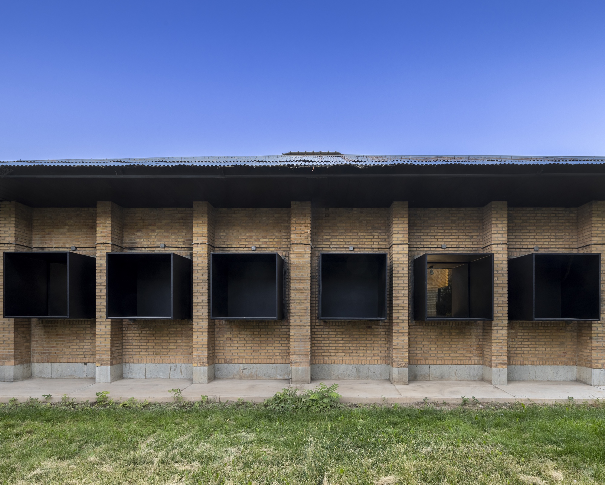 Facade with yellow brick columns and black metal-framed windows under a corrugated metal roof edge