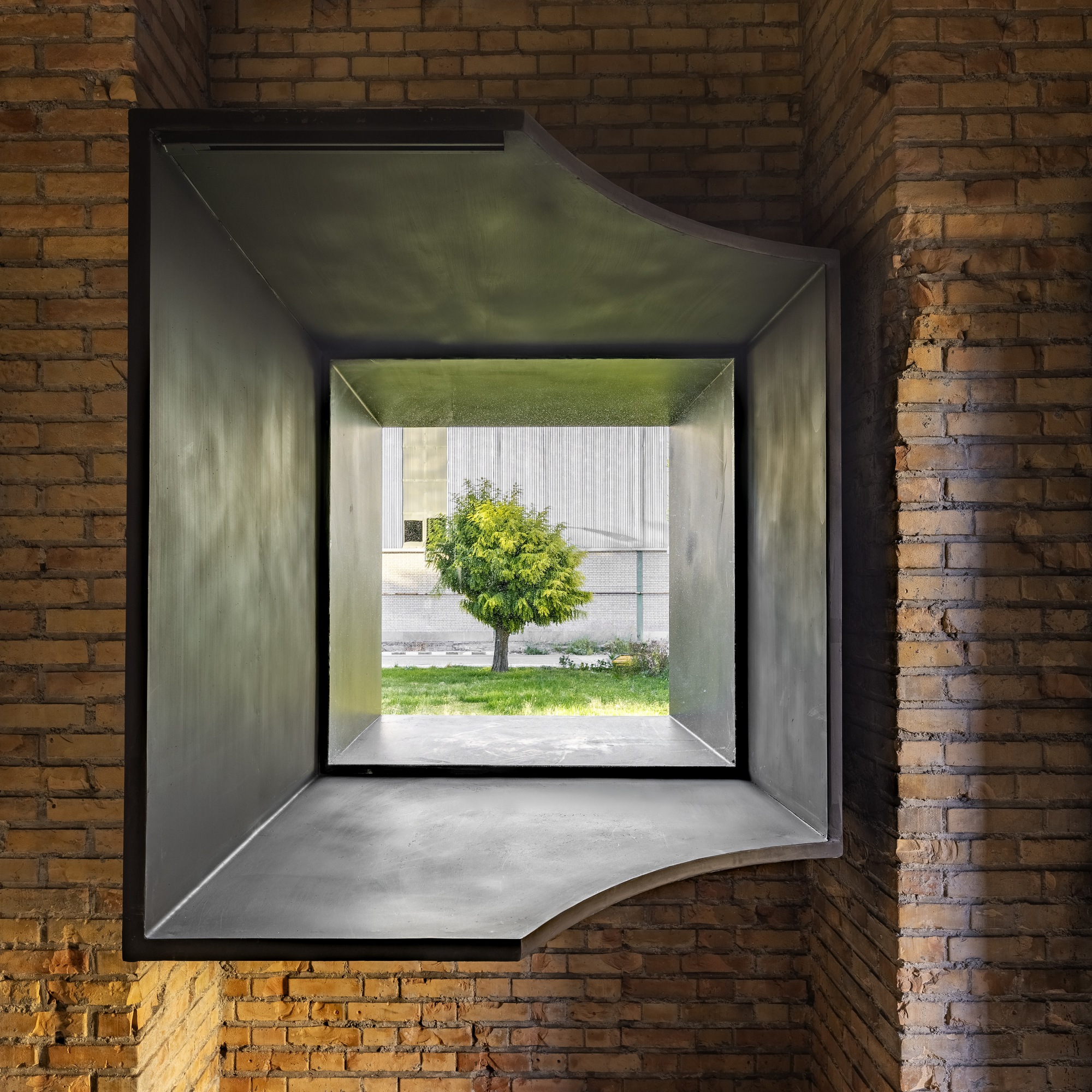 Deep window opening framing a tree in the courtyard through layered metal and concrete reveals