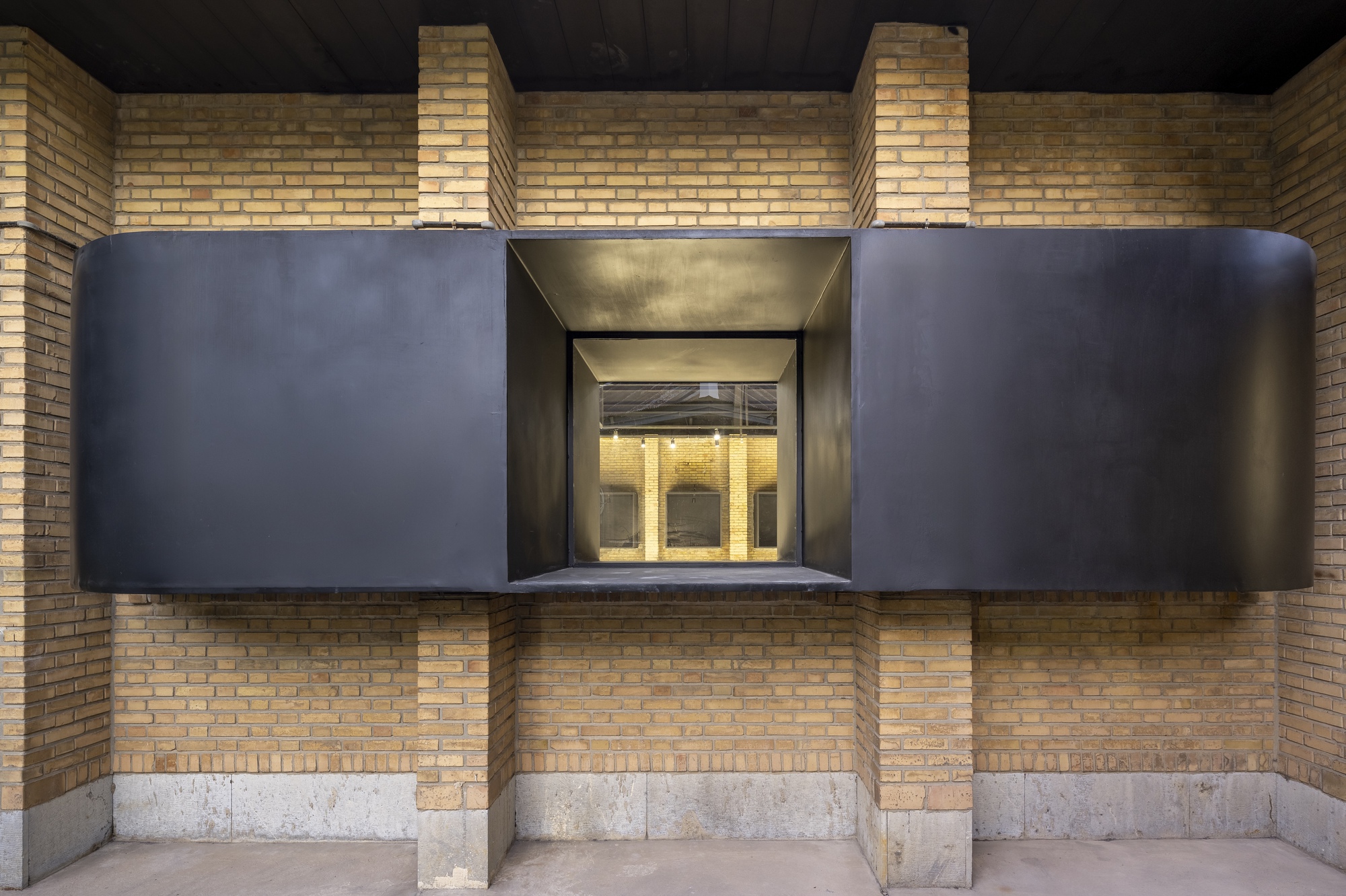 Frontal view of the projecting black steel bay window set within yellow brick courtyard walls