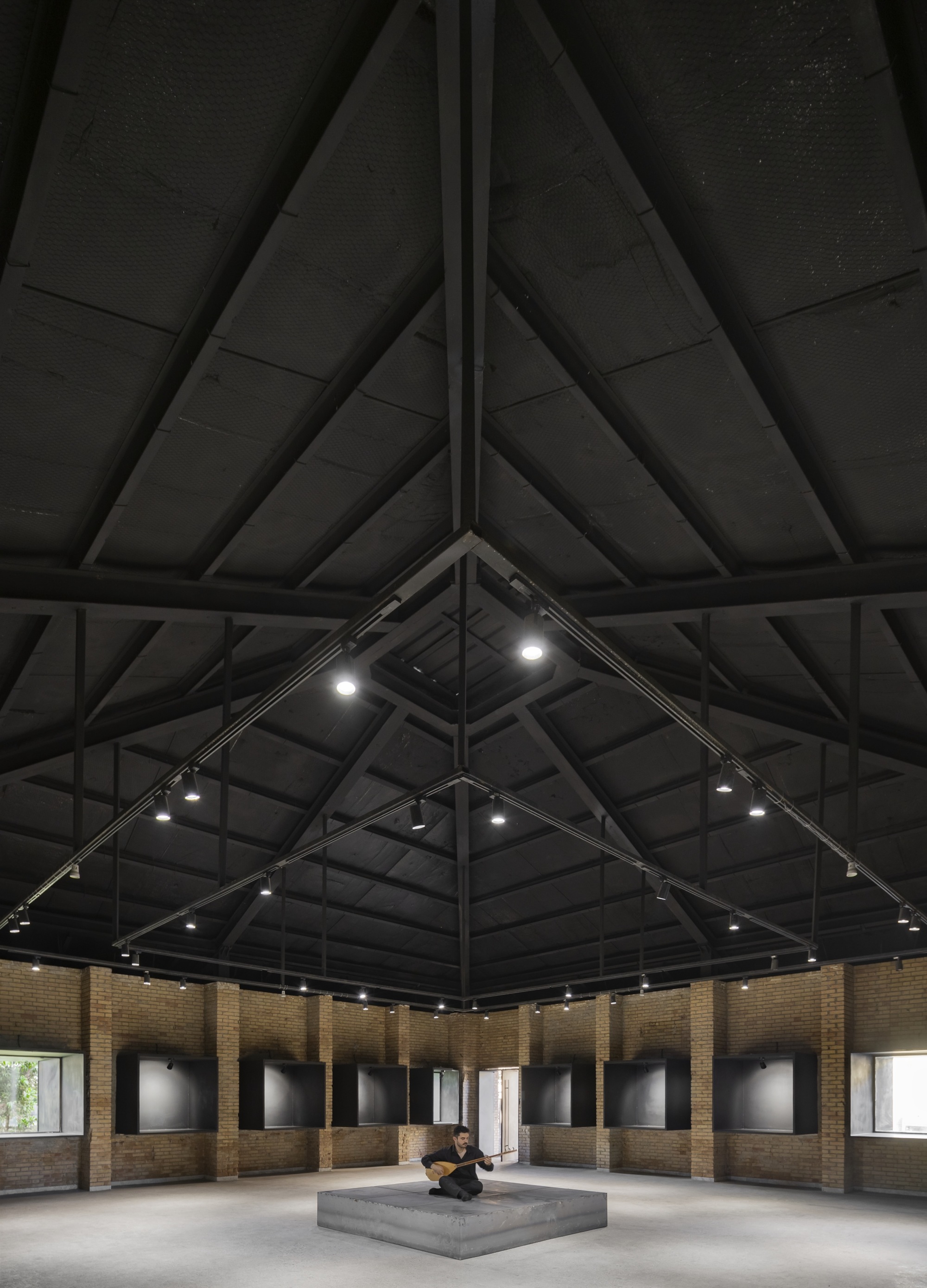 Upward view of the pyramidal timber roof structure with track lighting and concrete plinth below