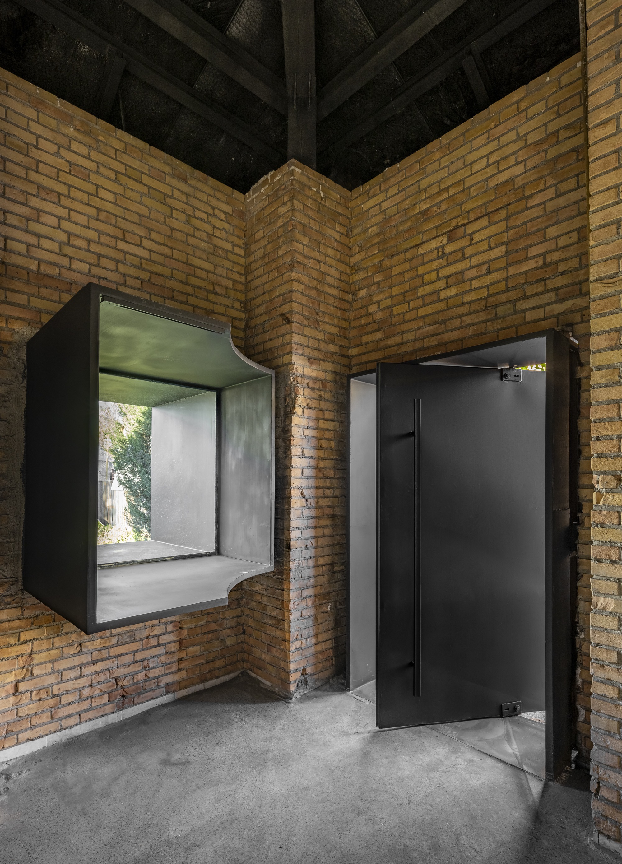 Corner courtyard with yellow brick walls, black timber ceiling and two black-framed box windows with a concrete floor