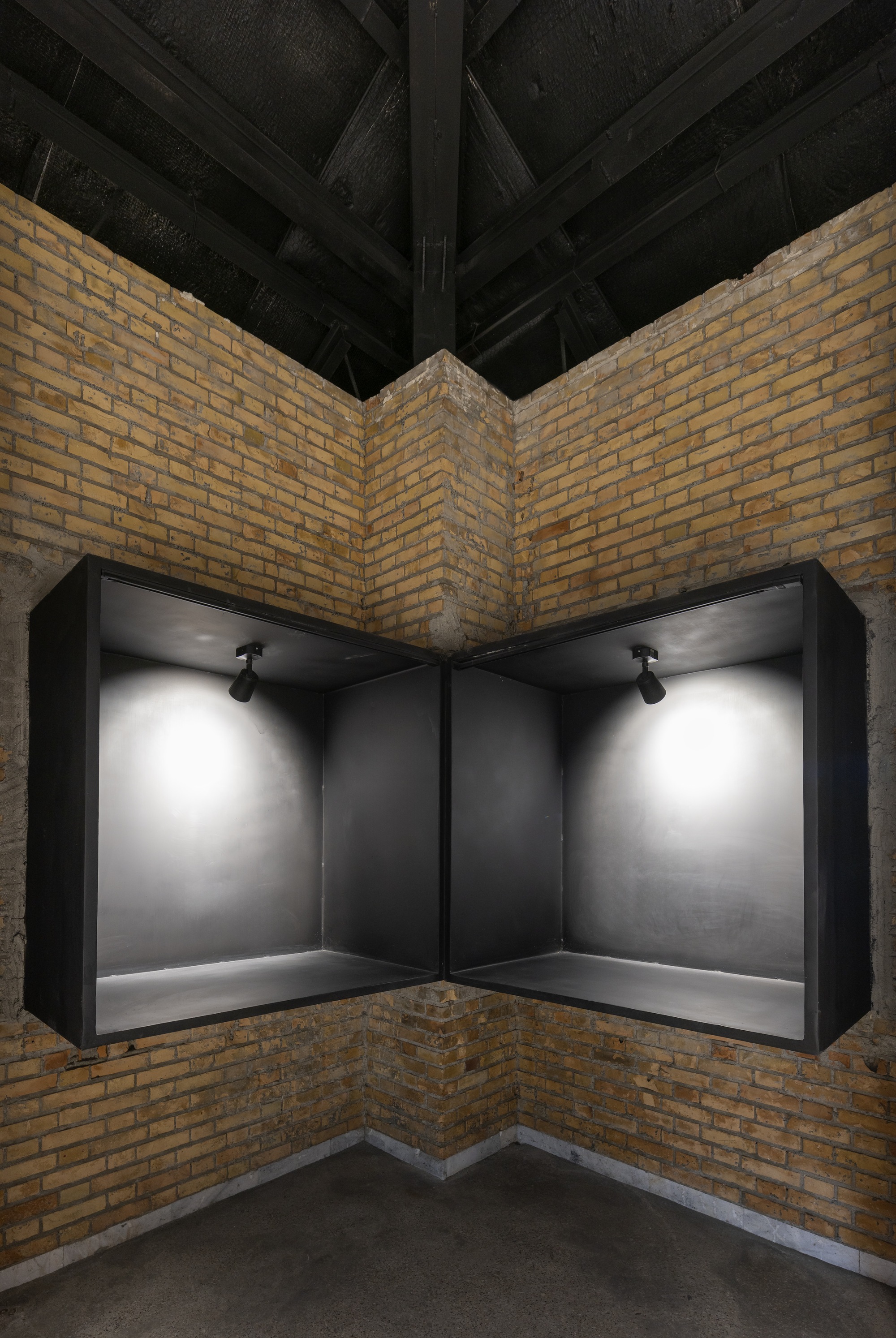 Corner display niche with black metal frame and spotlights set into yellow brick walls under exposed timber beams