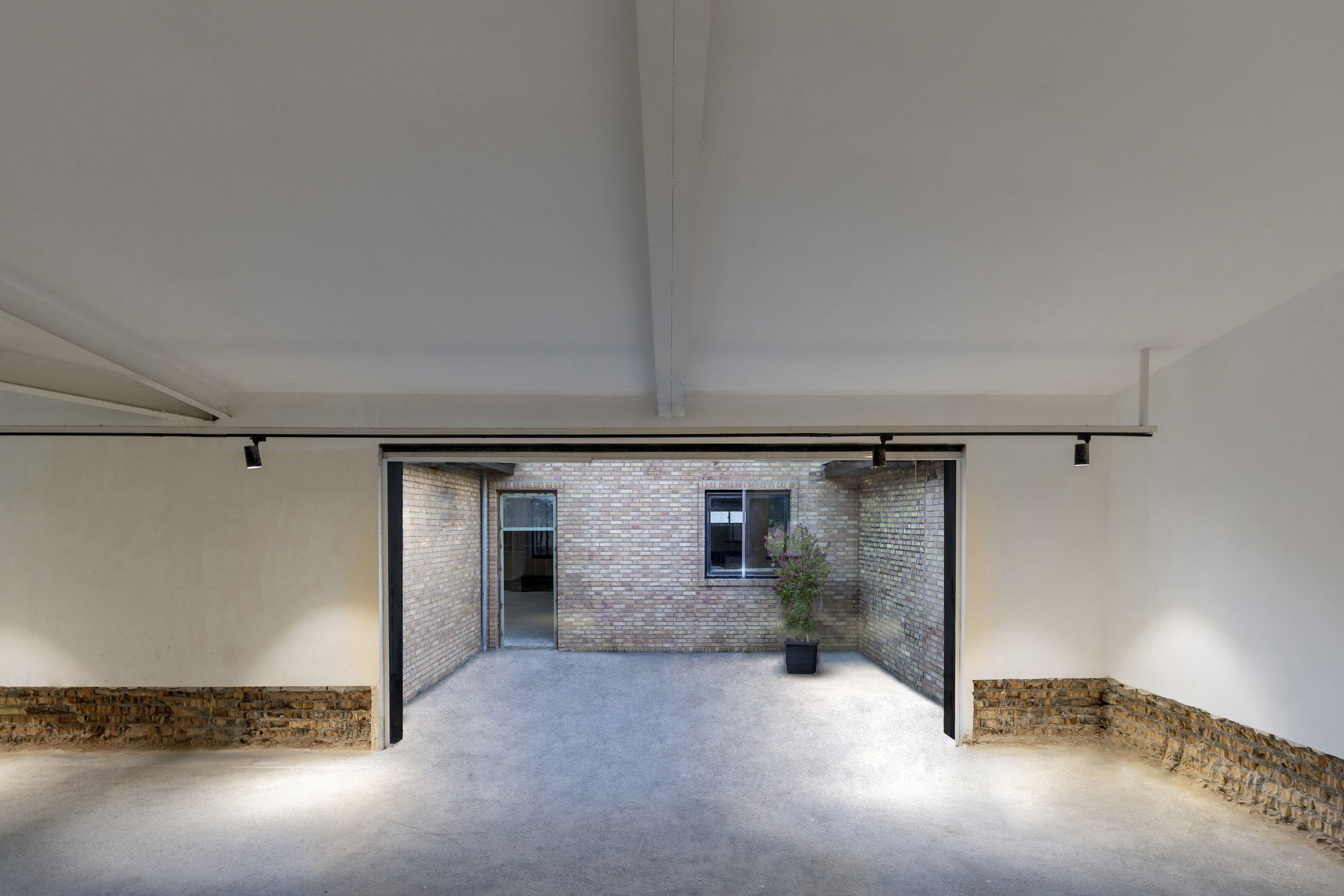 Interior gallery space with large opening framing a brick courtyard with a potted plant visible outside