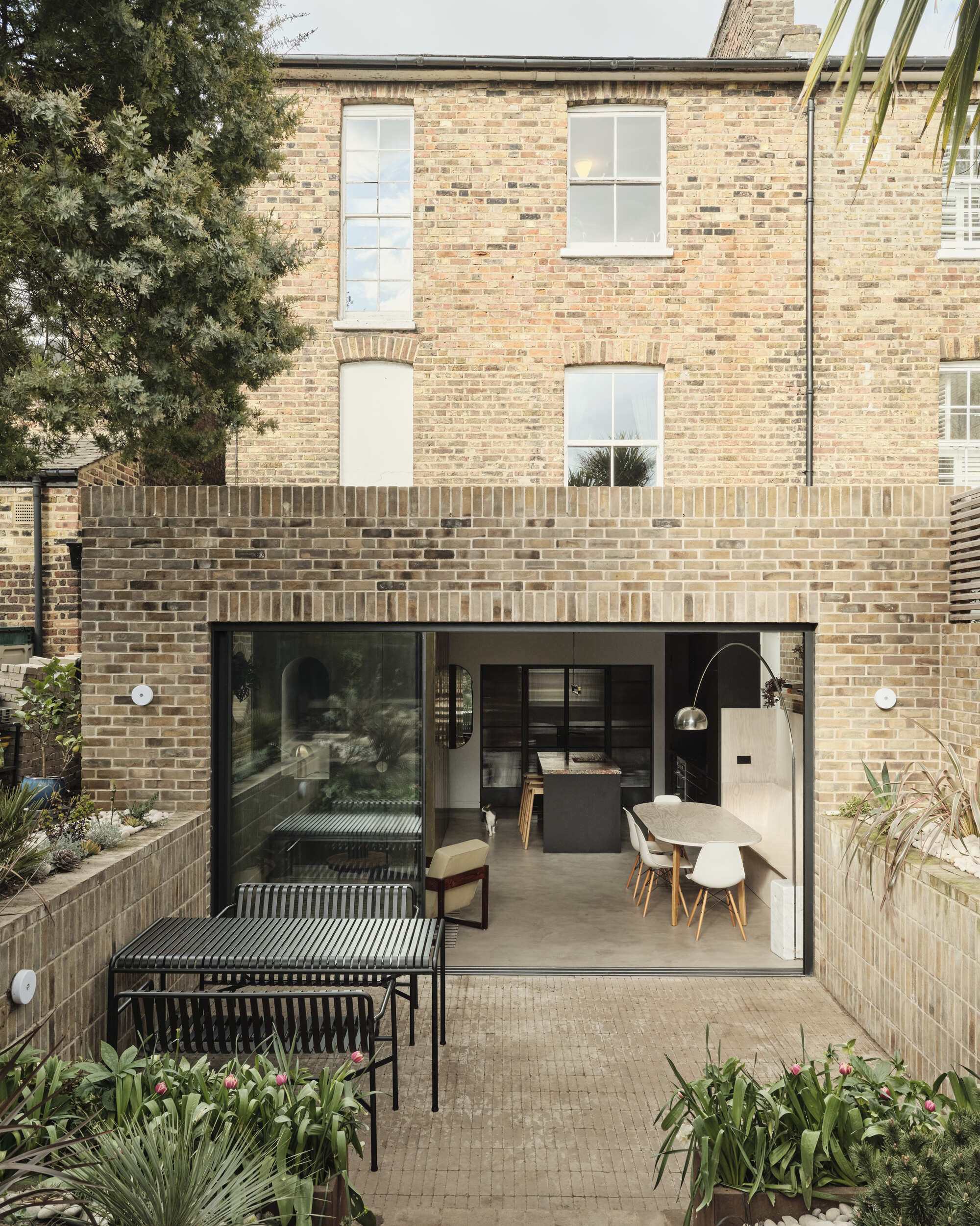 Garden view showing the rear extension with sliding glass doors beneath the original brick house