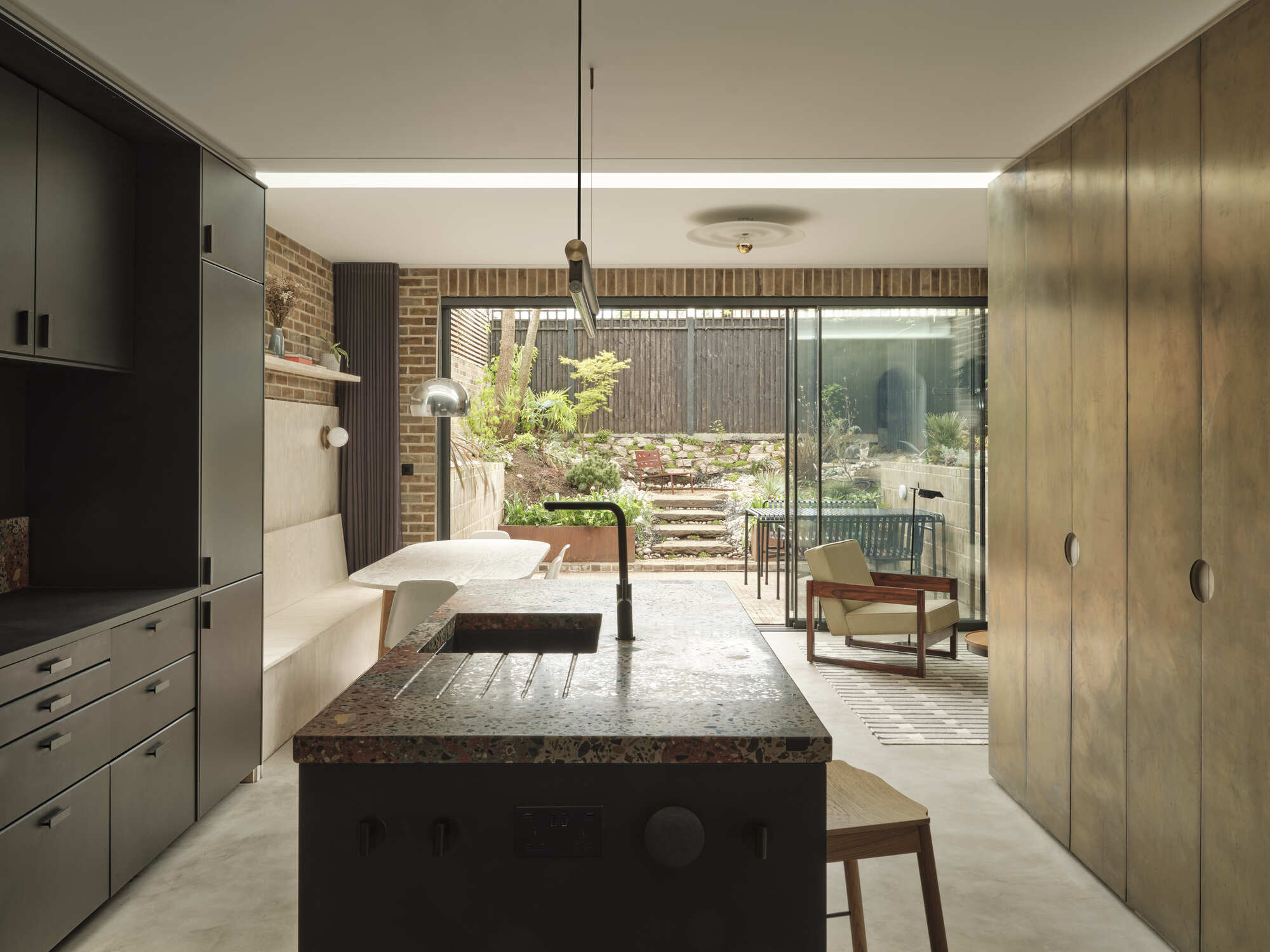 Kitchen island with terrazzo countertop looking through to the planted rear garden with timber steps