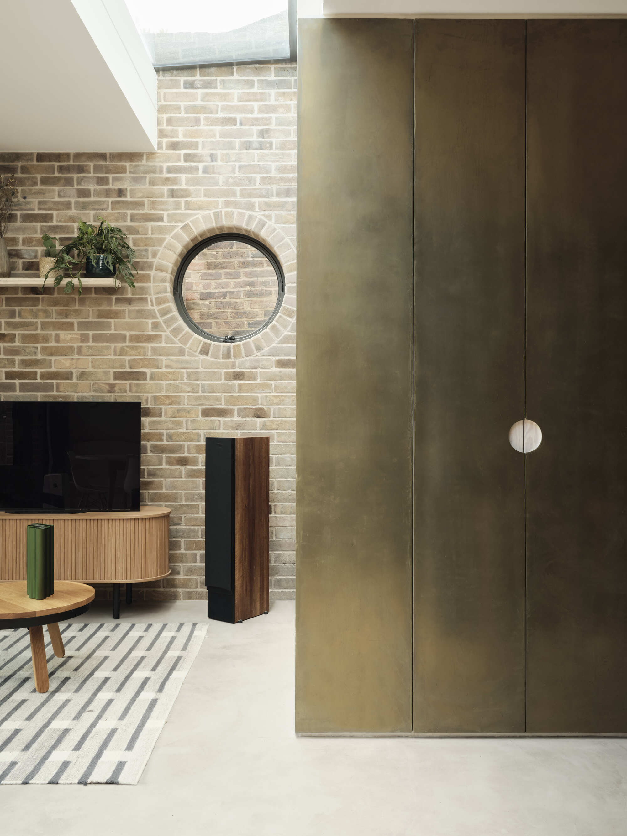 Living space showing tall brass-clad joinery beside a buff brick fireplace wall with circular window