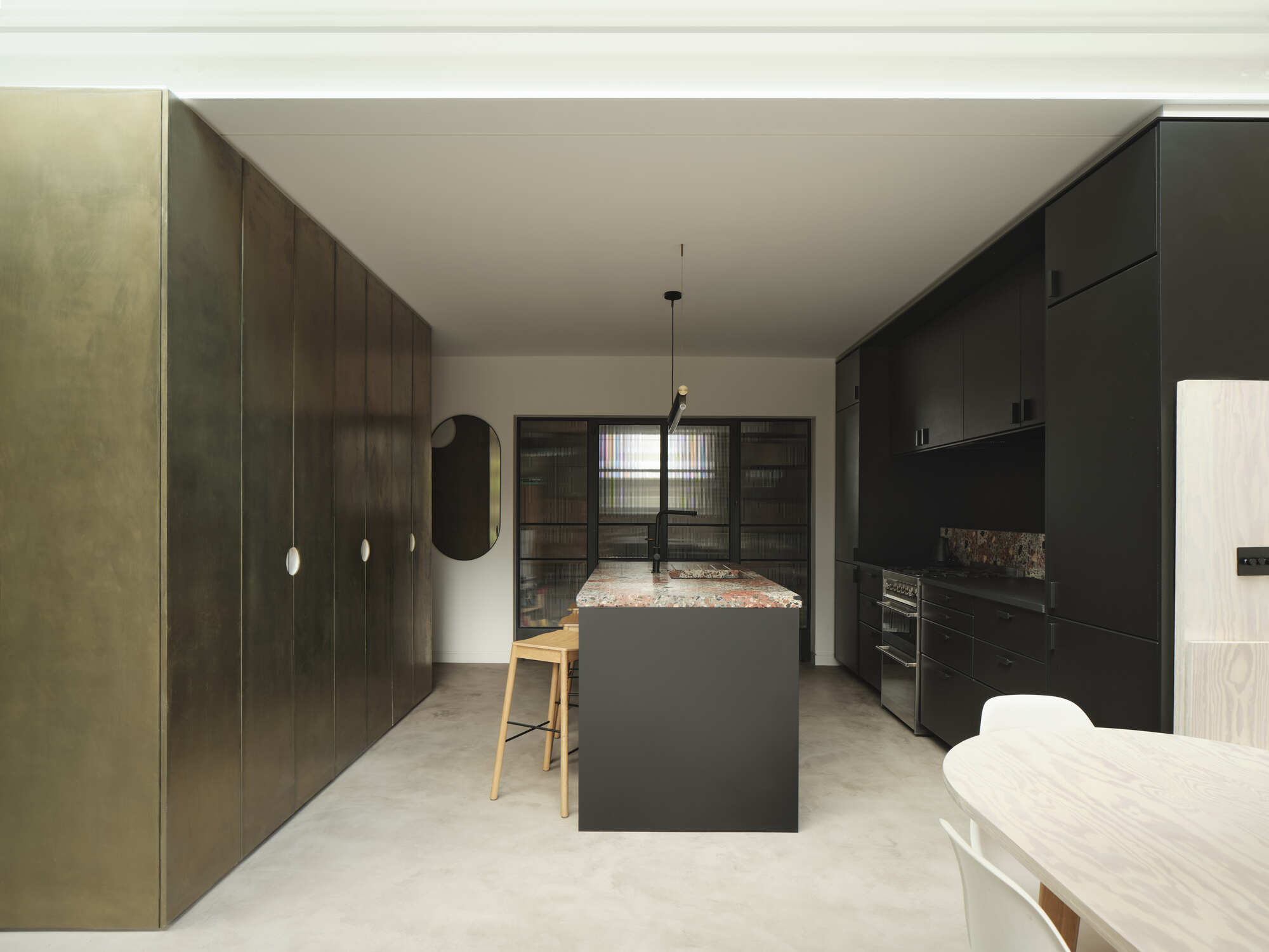 Kitchen with dark timber cabinetry, terrazzo island bench and pale polished concrete flooring